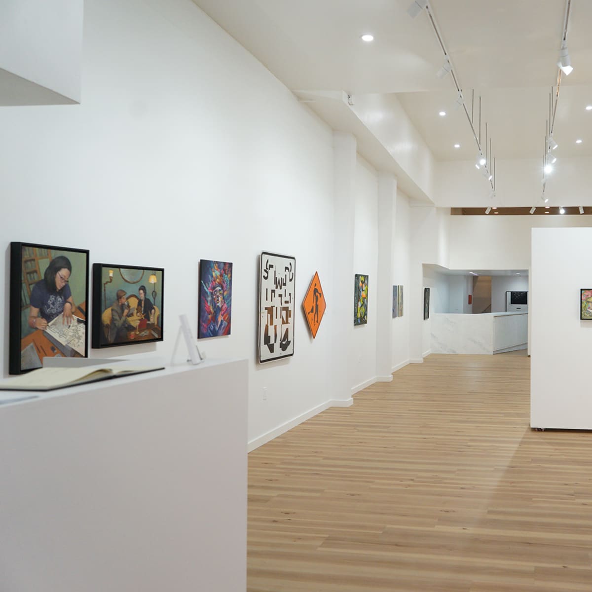 An art gallery interior with framed artworks displayed on the white walls and wooden flooring.
