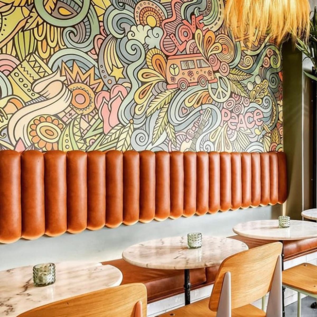 A brightly decorated café interior featuring a colorful mural, palm fronds, and round tables with wooden chairs.