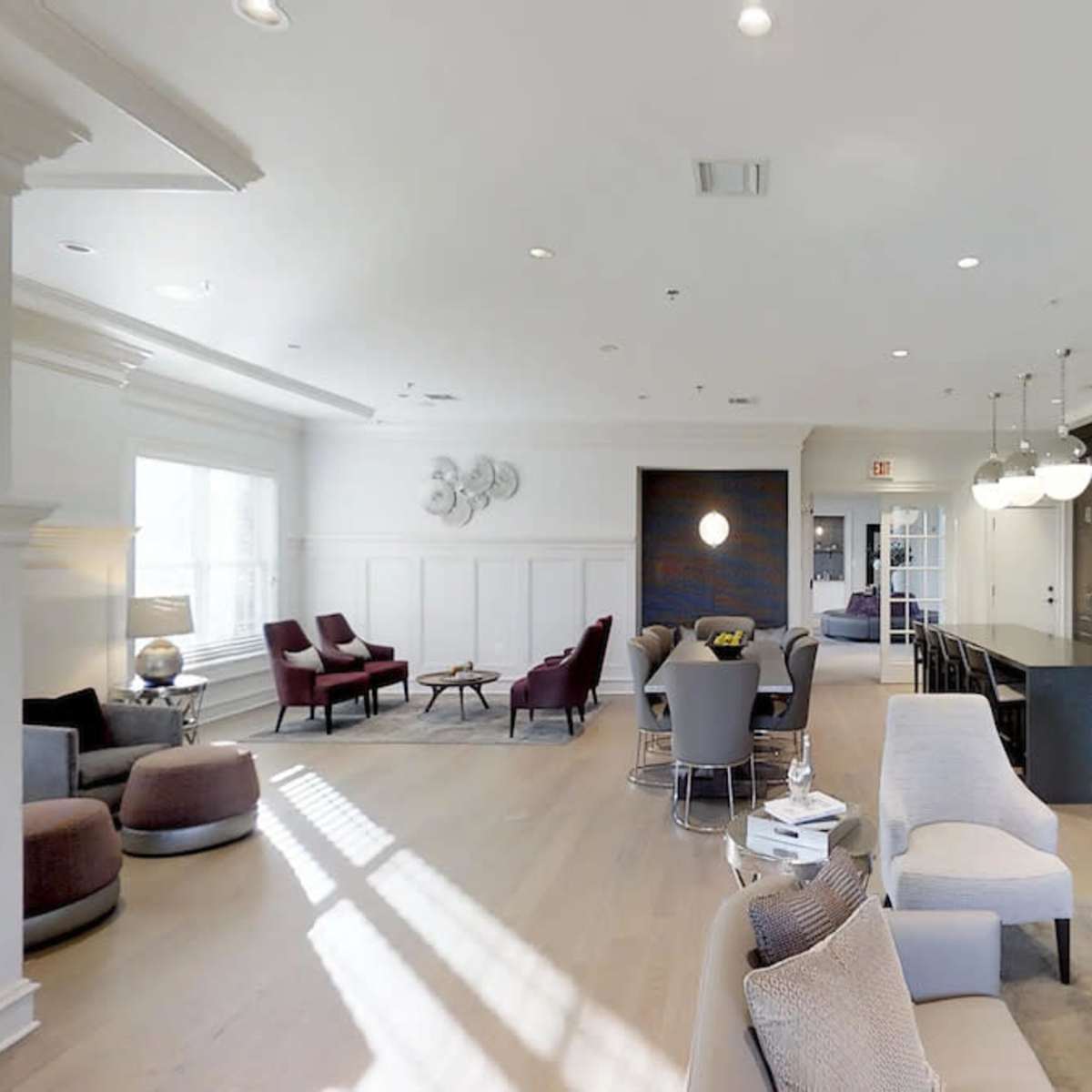 A spacious, modern common area with seating arrangements, a kitchen bar, and large windows allowing natural light to fill the room.