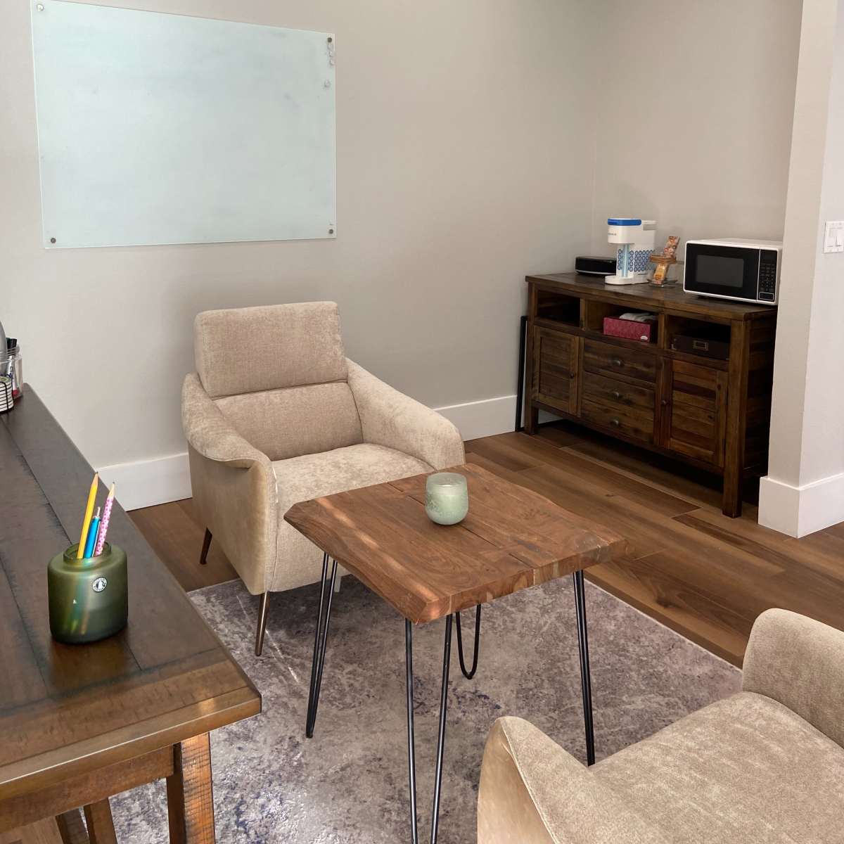 A small office space with two beige chairs, a wooden table, a dark wooden cabinet, a microwave, and a whiteboard mounted on the wall.