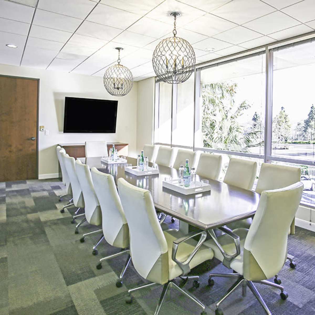 A modern conference room with a long table, white ergonomic chairs, and large windows allowing natural light to enter.