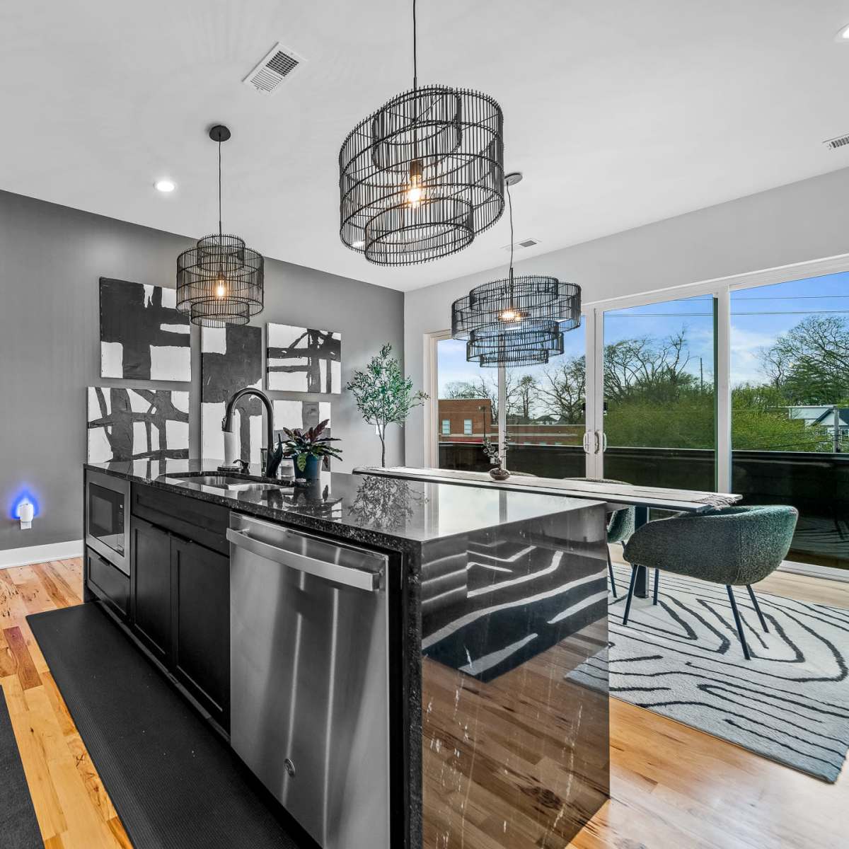 A modern kitchen features a central island with a black countertop, sleek appliances, and large windows overlooking a deck.