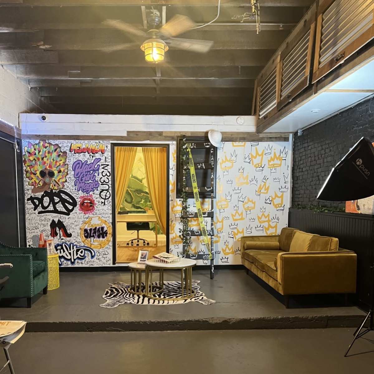 A creatively decorated indoor space featuring a yellow curtain, graffiti-covered walls, a brown sofa, and a green chair with a lighting setup.