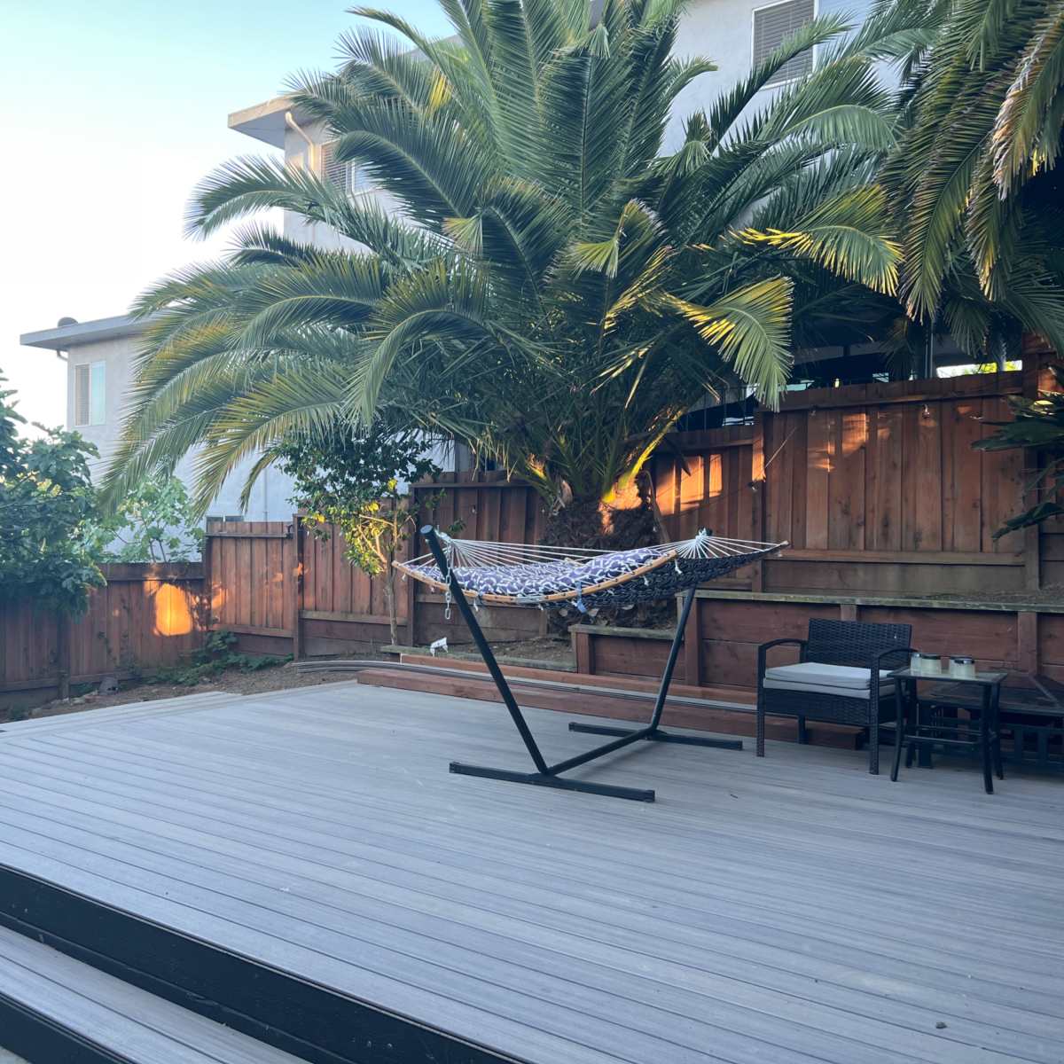A wooden deck features a hammock hanging between palm trees, with a seating area in the background.