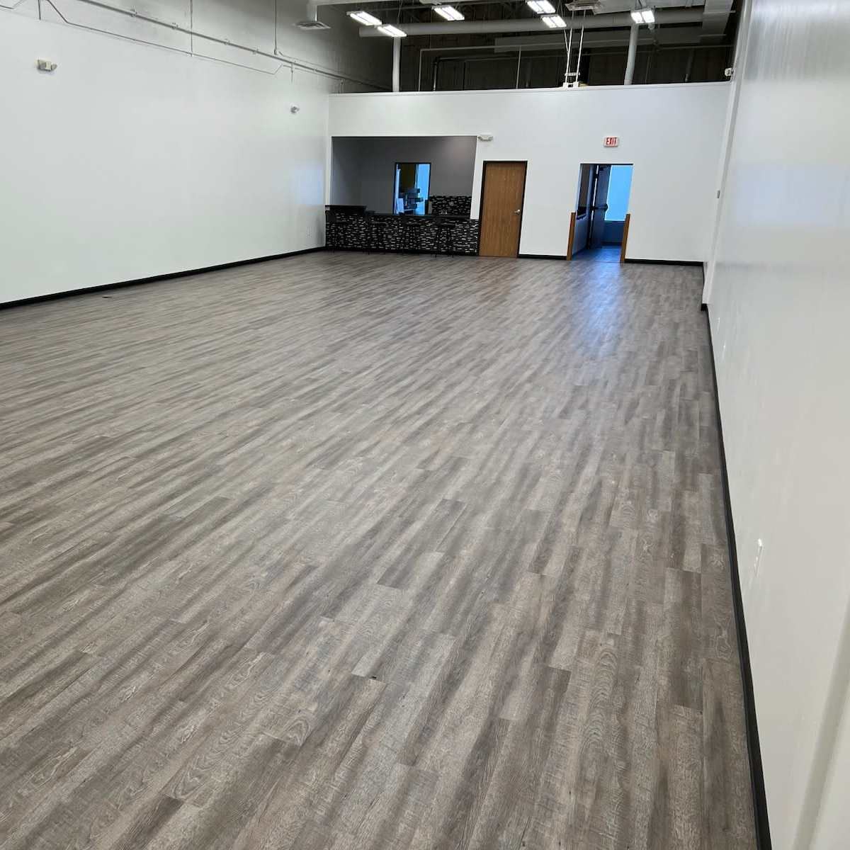 A spacious, empty indoor area with a smooth wooden floor and white walls.