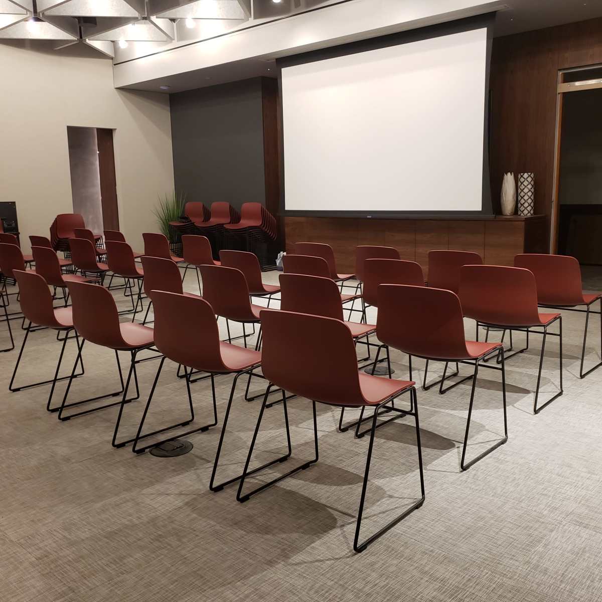 A conference room with several rows of empty red chairs facing a projected screen.