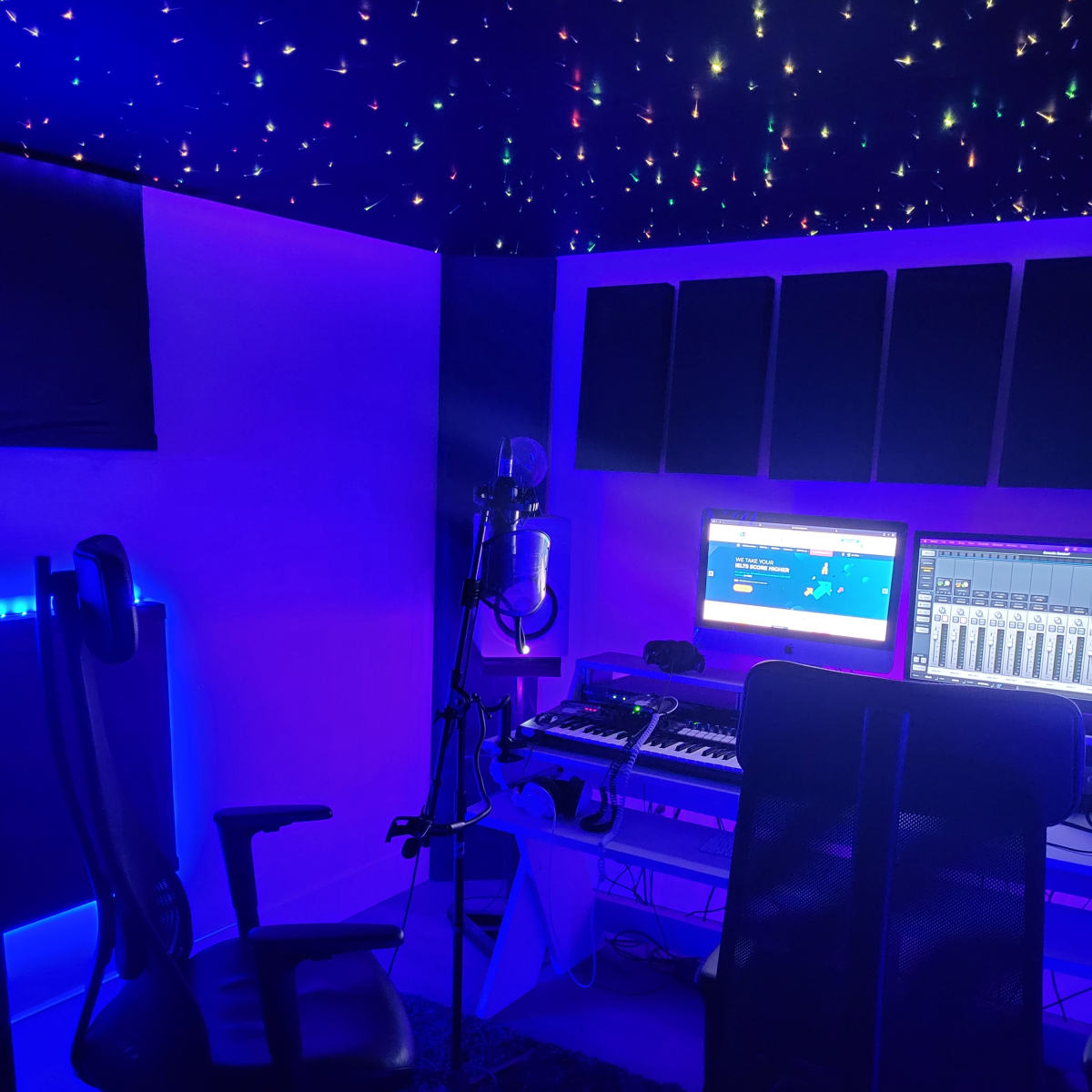 A dimly lit music studio featuring a microphone, keyboard, computer monitors, and a chair, all surrounded by a starry ceiling.