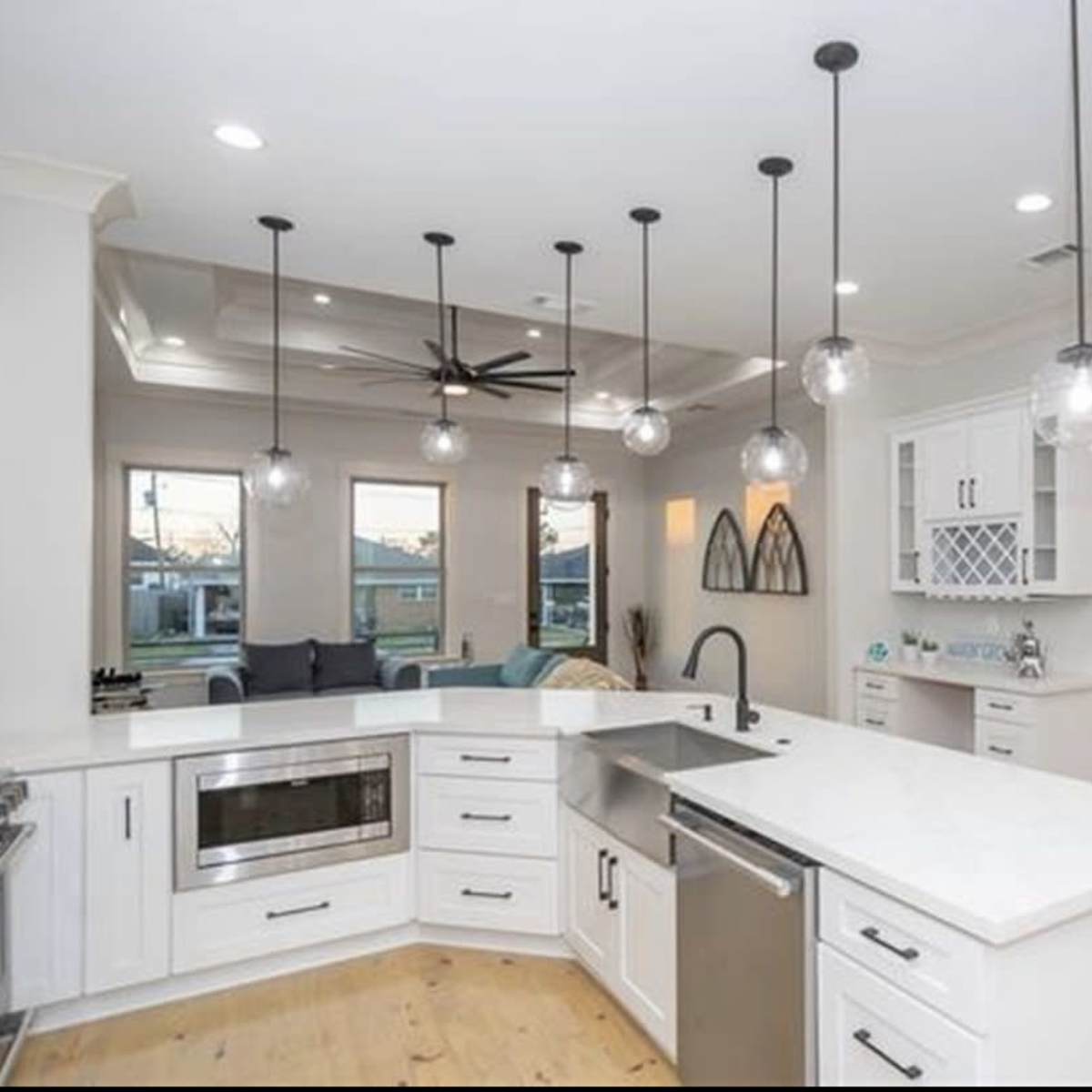 A modern kitchen features white cabinetry, a large island with a sink, and multiple pendant lights hanging from the ceiling.