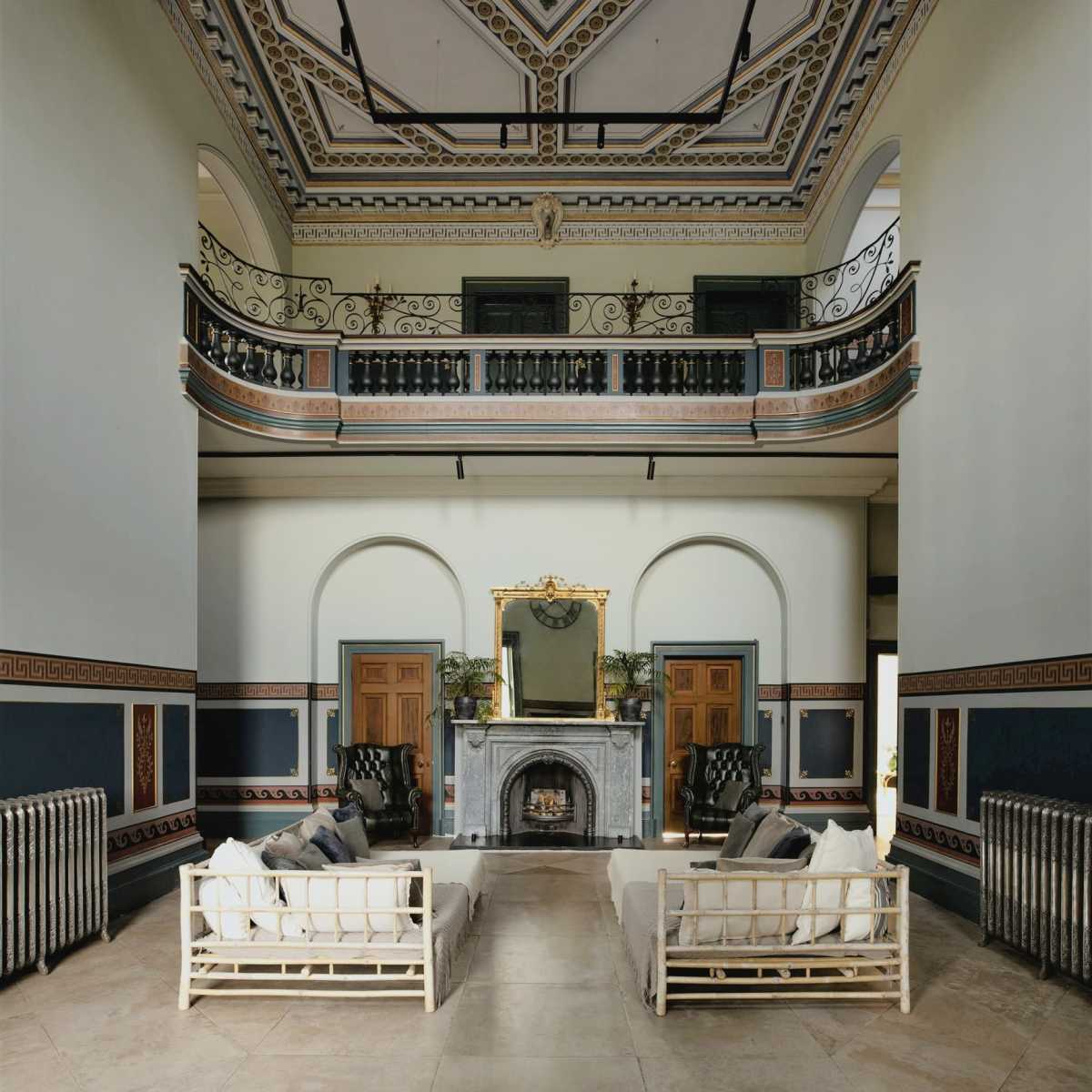 A spacious, grand living area featuring high ceilings, classical moldings, and two sets of white sofas arranged around a central fireplace.