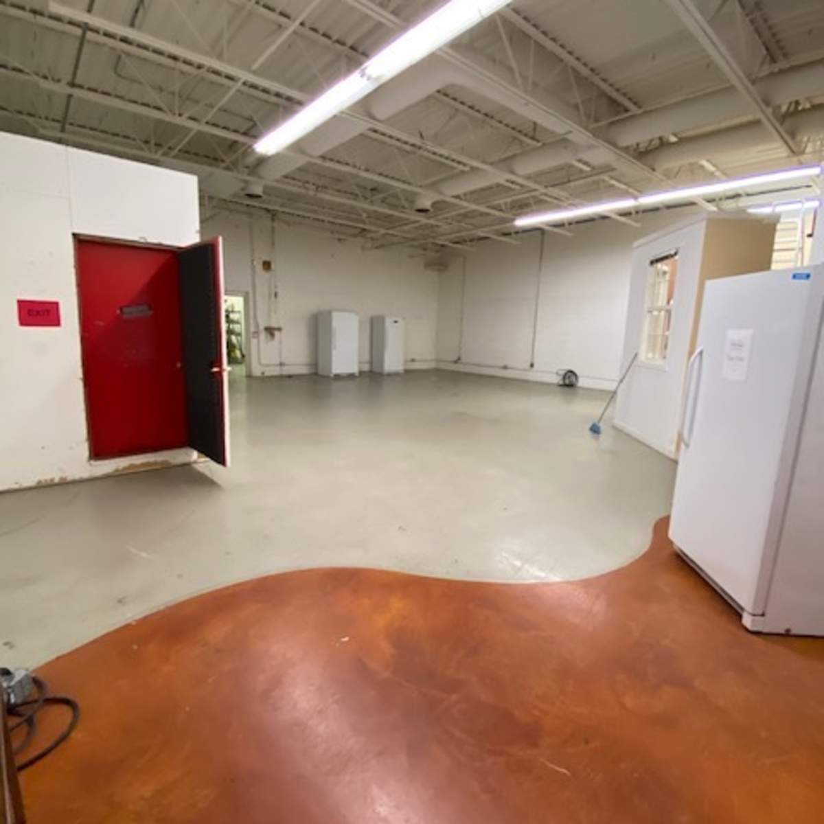 An empty room with a red door, two refrigerators, and a polished concrete floor.