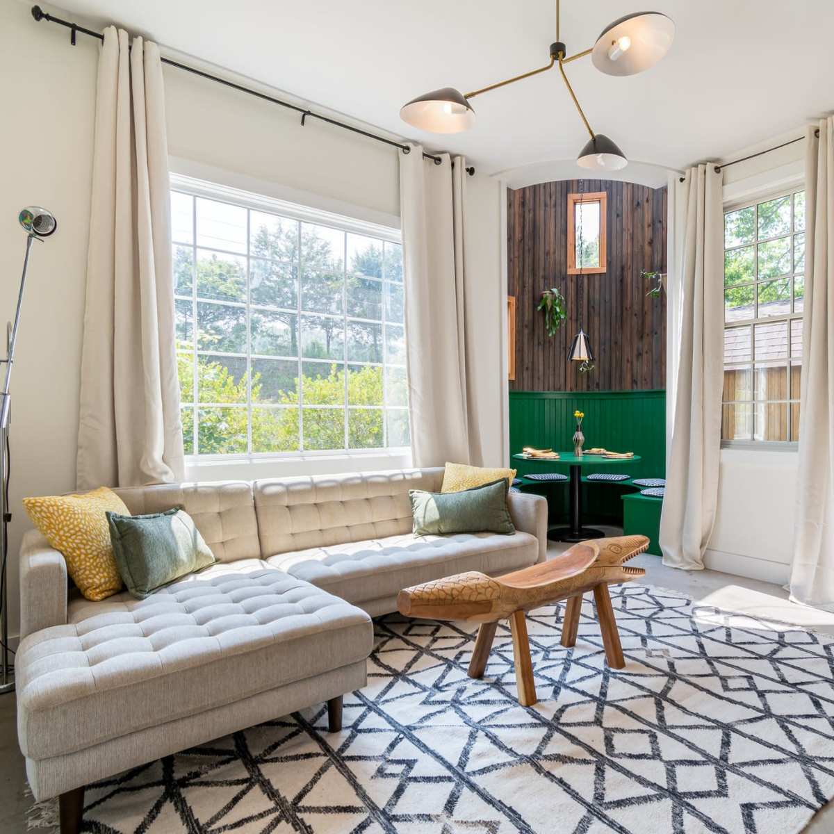 A modern living room features a light-colored sofa, a wooden coffee table, and a bright blue door, with large windows allowing natural light to fill the space.