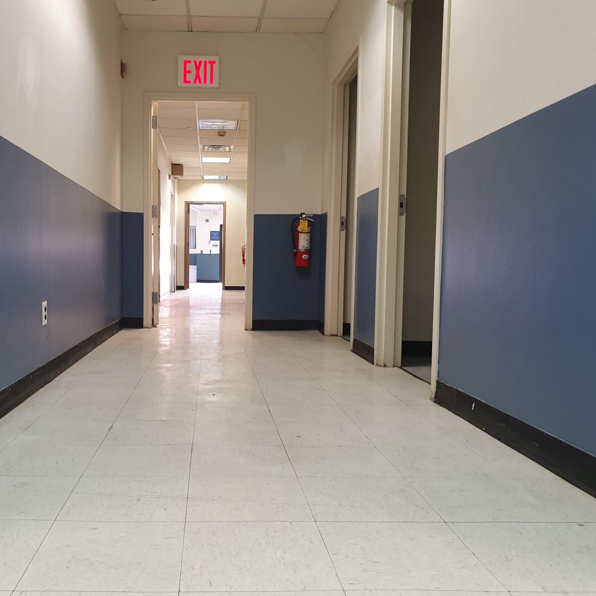 A long corridor with blue and white walls leads to an exit door at the far end.