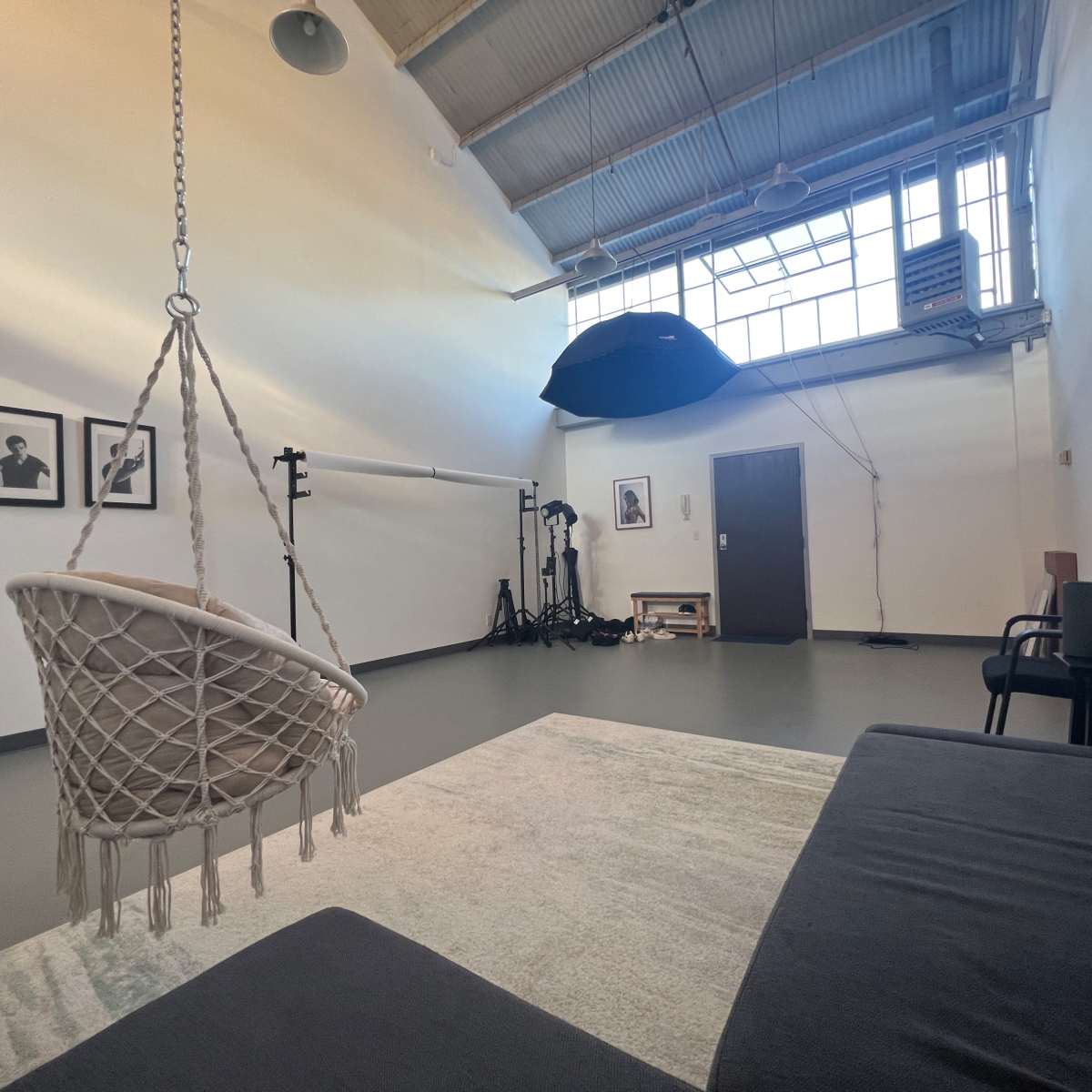 A spacious studio with a hanging chair, a sofa, framed photographs on the wall, and photography equipment in the background.