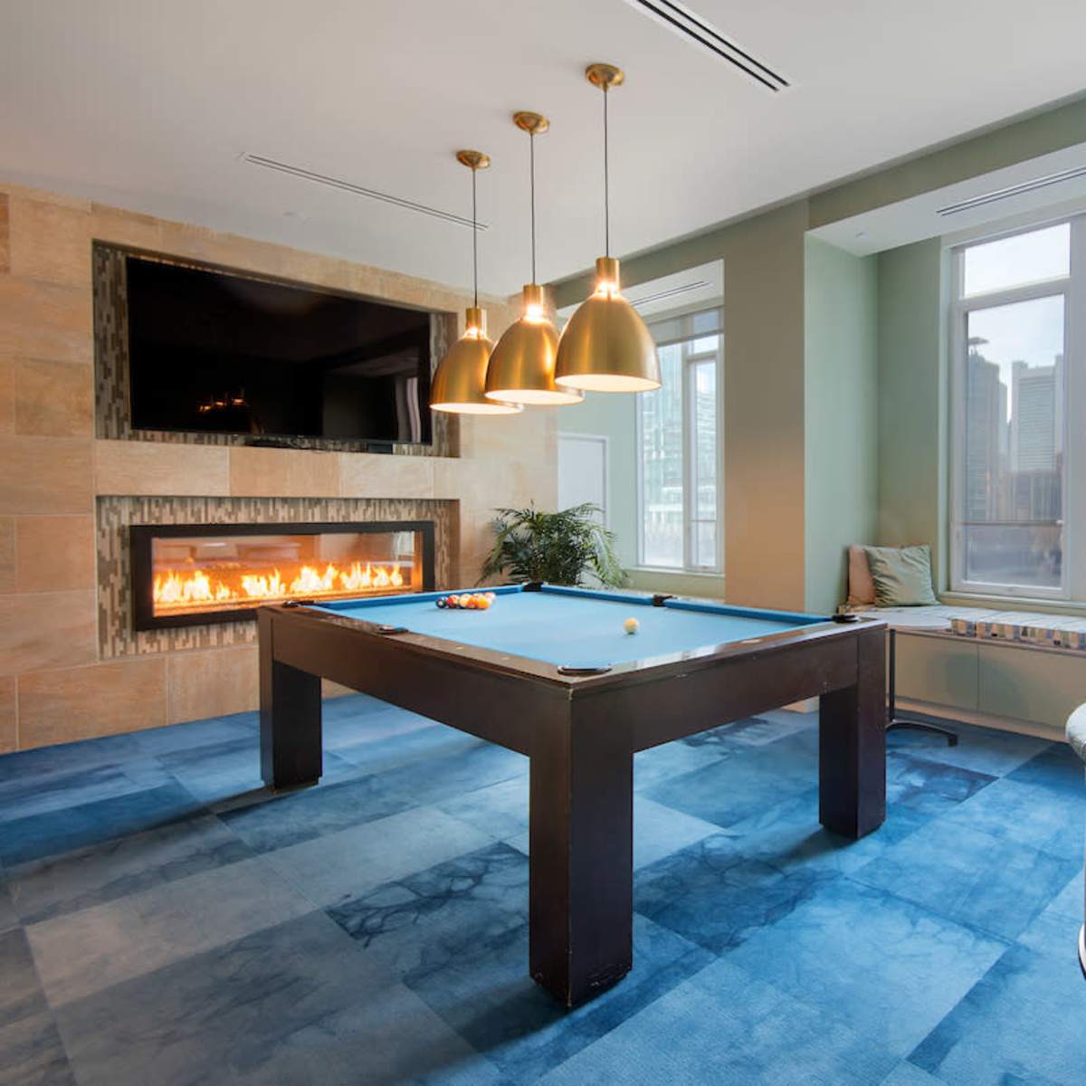 A modern game room featuring a pool table, a cozy seating area, and large windows showcasing a city skyline.