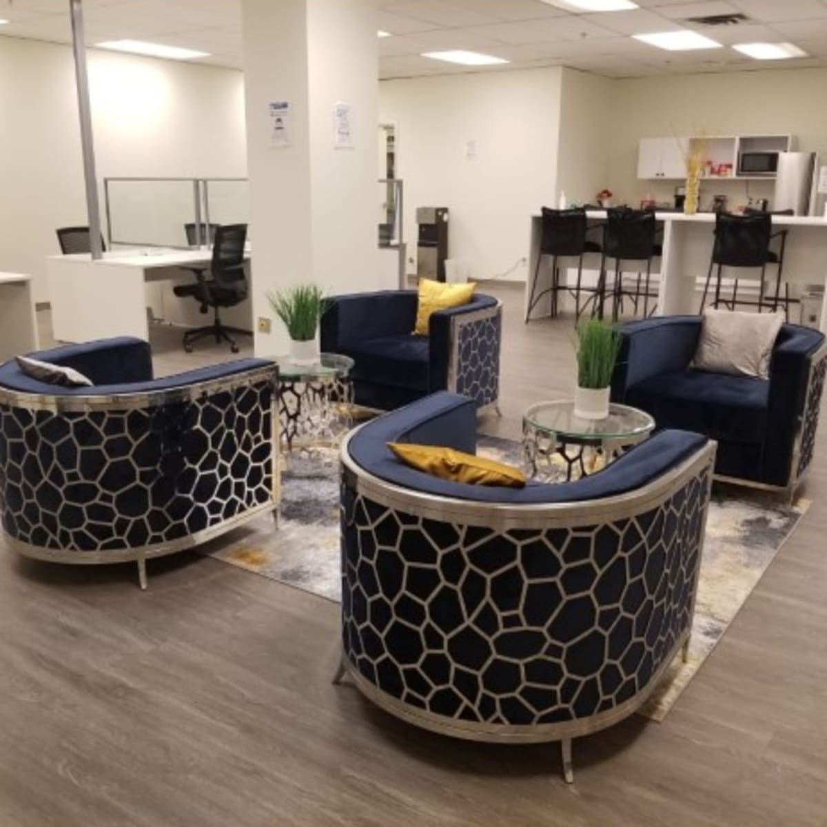 A modern office space features four circular chairs arranged around a small table, with a kitchenette visible in the background.