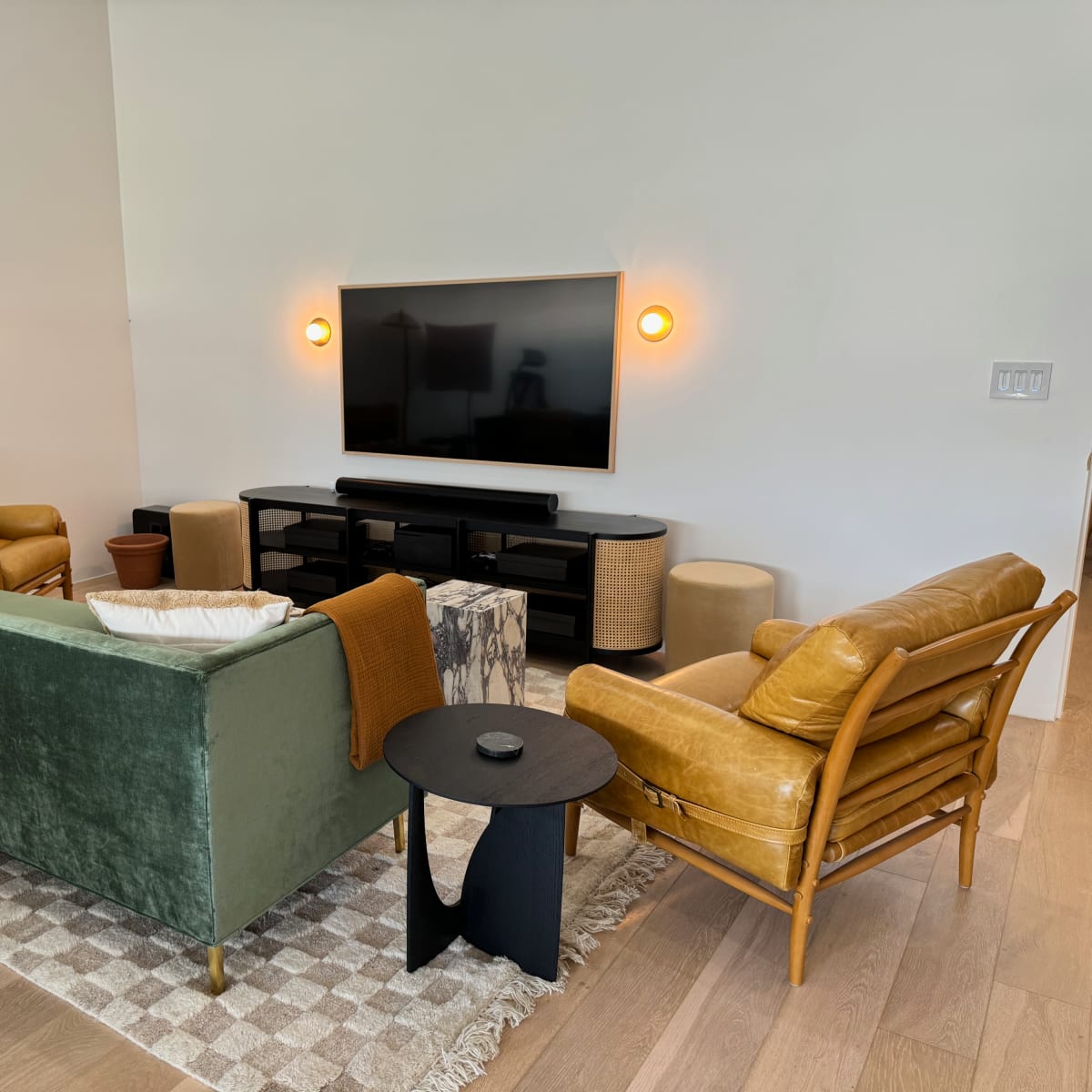 A modern living room featuring a green velvet sofa, a yellow leather chair, a black coffee table, and a mounted television on a white wall.