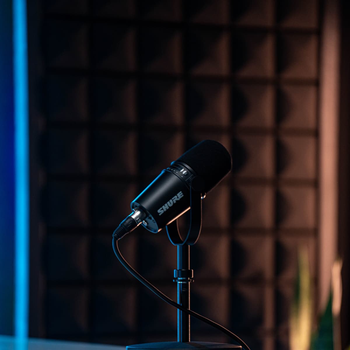 A black microphone on a stand is positioned on a table with a textured soundproof wall in the background.