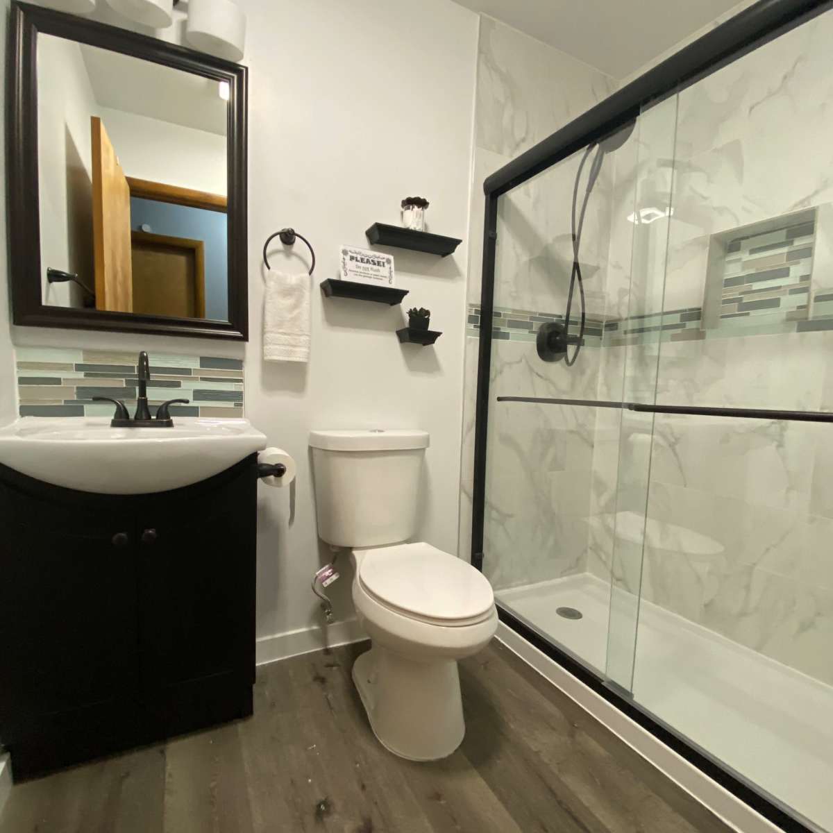 A modern bathroom featuring a shower, toilet, and sink with dark cabinetry and light-colored walls.