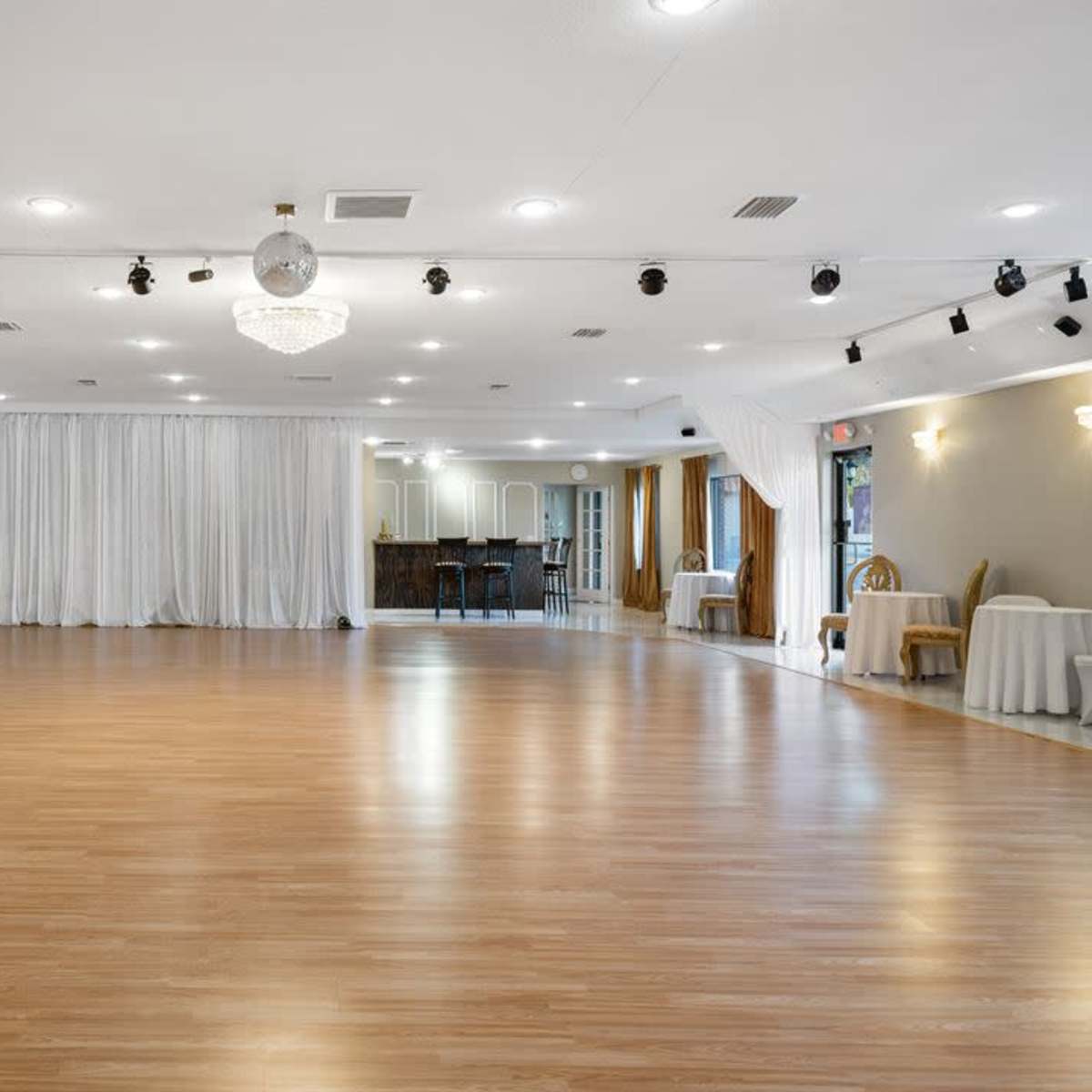 A spacious empty dance studio with wooden flooring,several light fixtures, and curtains in the background.