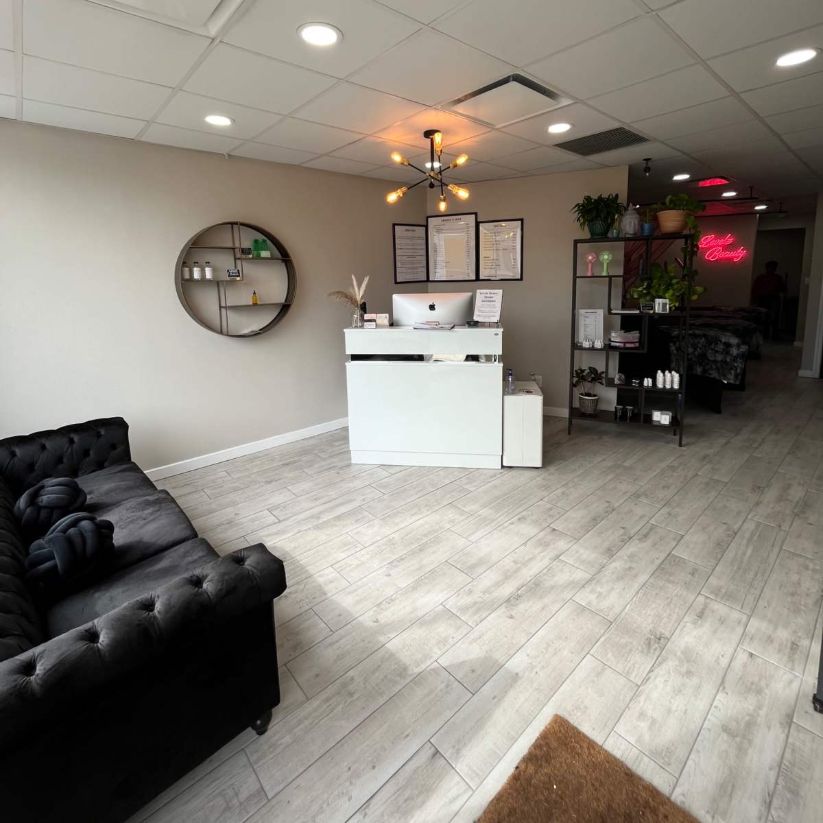 A modern reception area with a white front desk, a black tufted sofa, and various decorative items arranged on the walls and shelves.