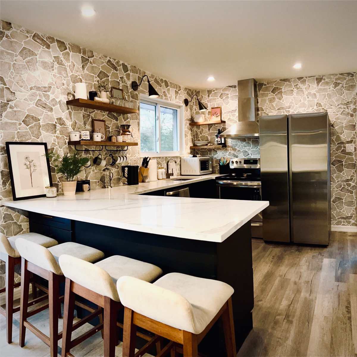 A modern kitchen features stone-patterned walls, a large island with seating, stainless steel appliances, and open shelving displaying kitchenware.