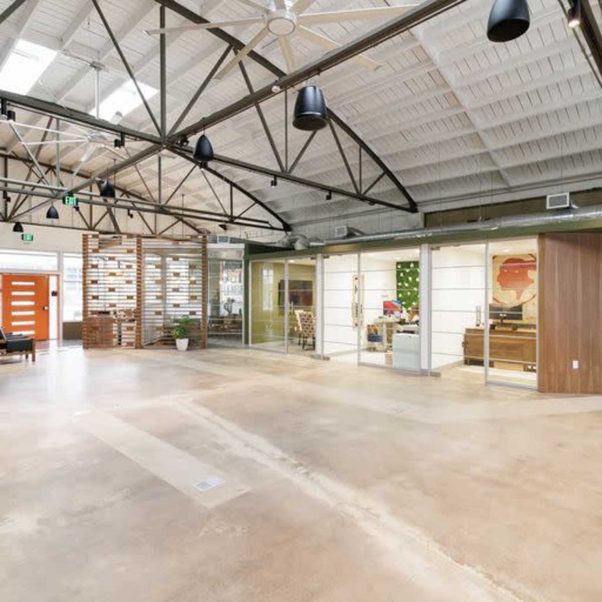 A spacious, modern office interior with high ceilings, exposed beams, and a mix of open and partitioned work areas.