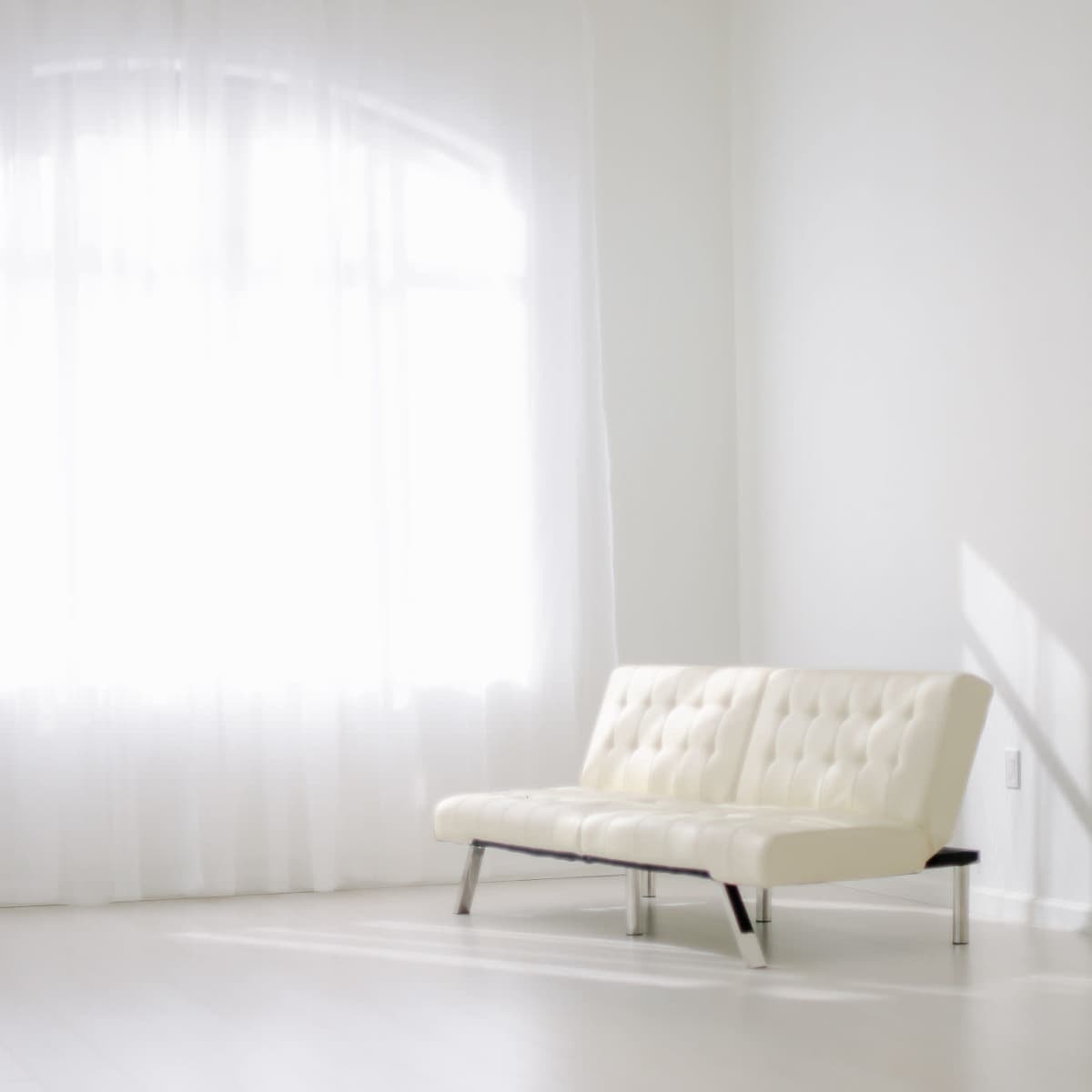 A white couch is positioned in a bright room with large windows and sheer curtains.