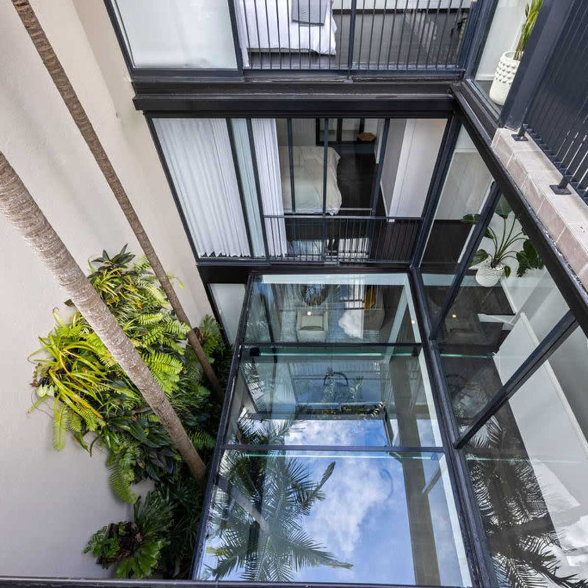 An overhead view shows a glass-walled courtyard surrounded by modern buildings with palm trees and lush greenery.