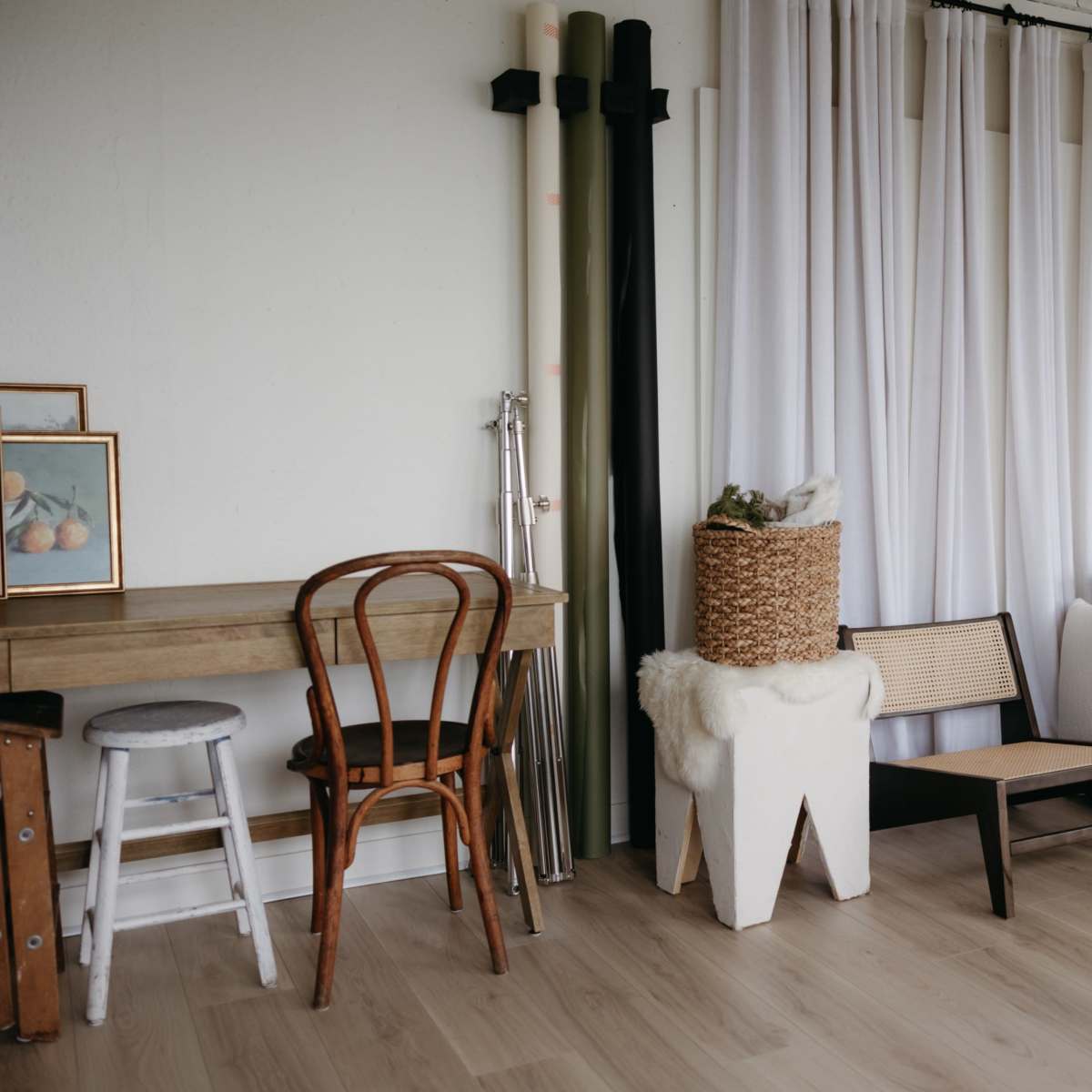 A minimalist interior space featuring a wooden table and chairs, a white couch, a basket, and backdrop poles with drapery.