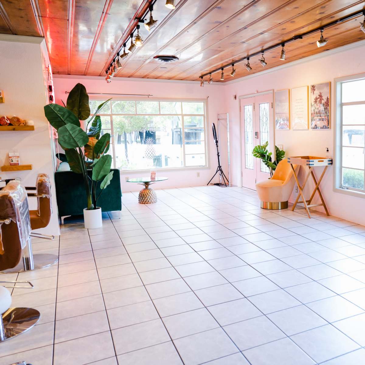 A spacious, well-lit interior with tiled flooring, large windows, and minimal furniture including a plant, a chair, and a table.