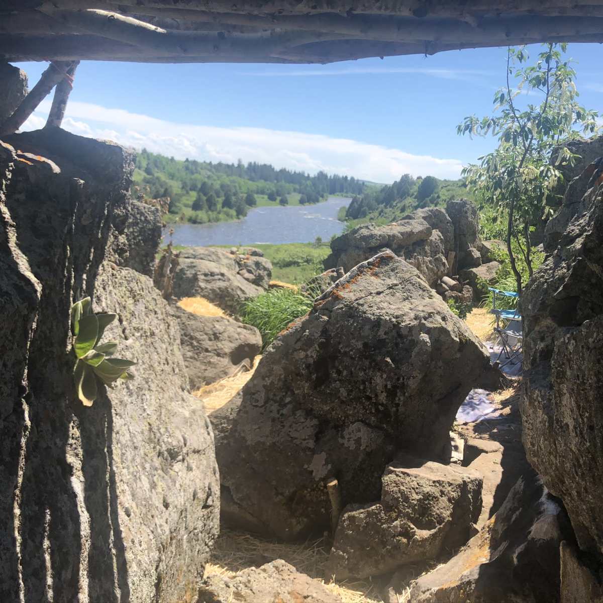 A view from a rocky shelter overlooking a river and green landscape under a clear sky.