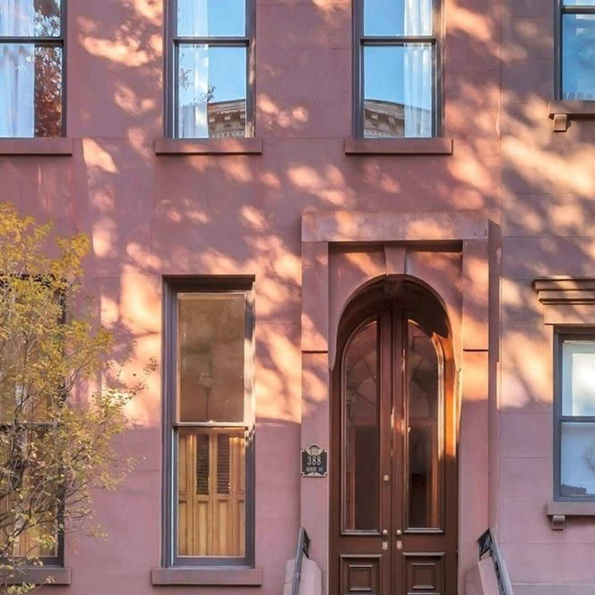 A brownstone building with a set of stairs leading up to a large arched wooden door framed by multiple windows.