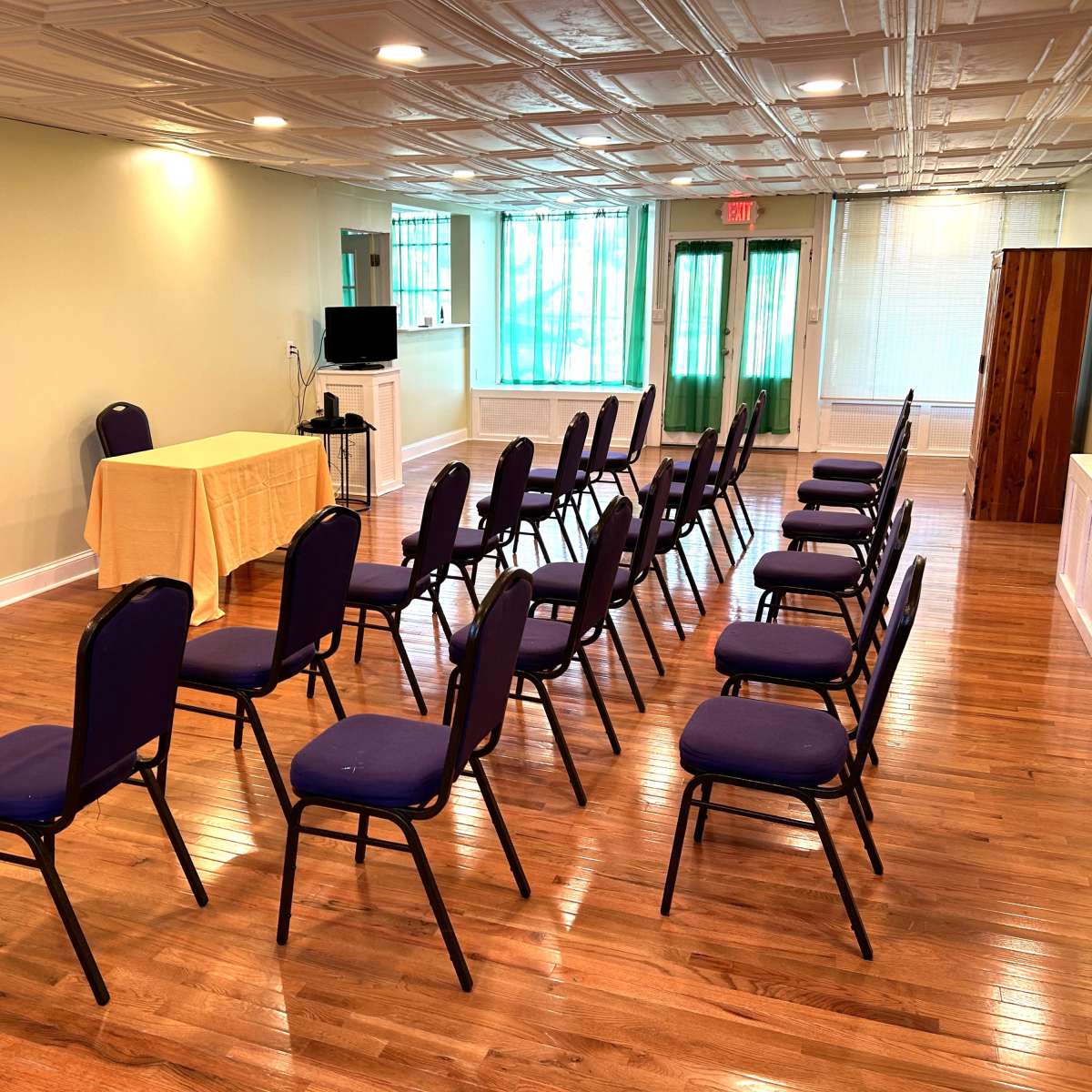 A meeting room is set up with rows of purple chairs facing a table covered with a yellow cloth.