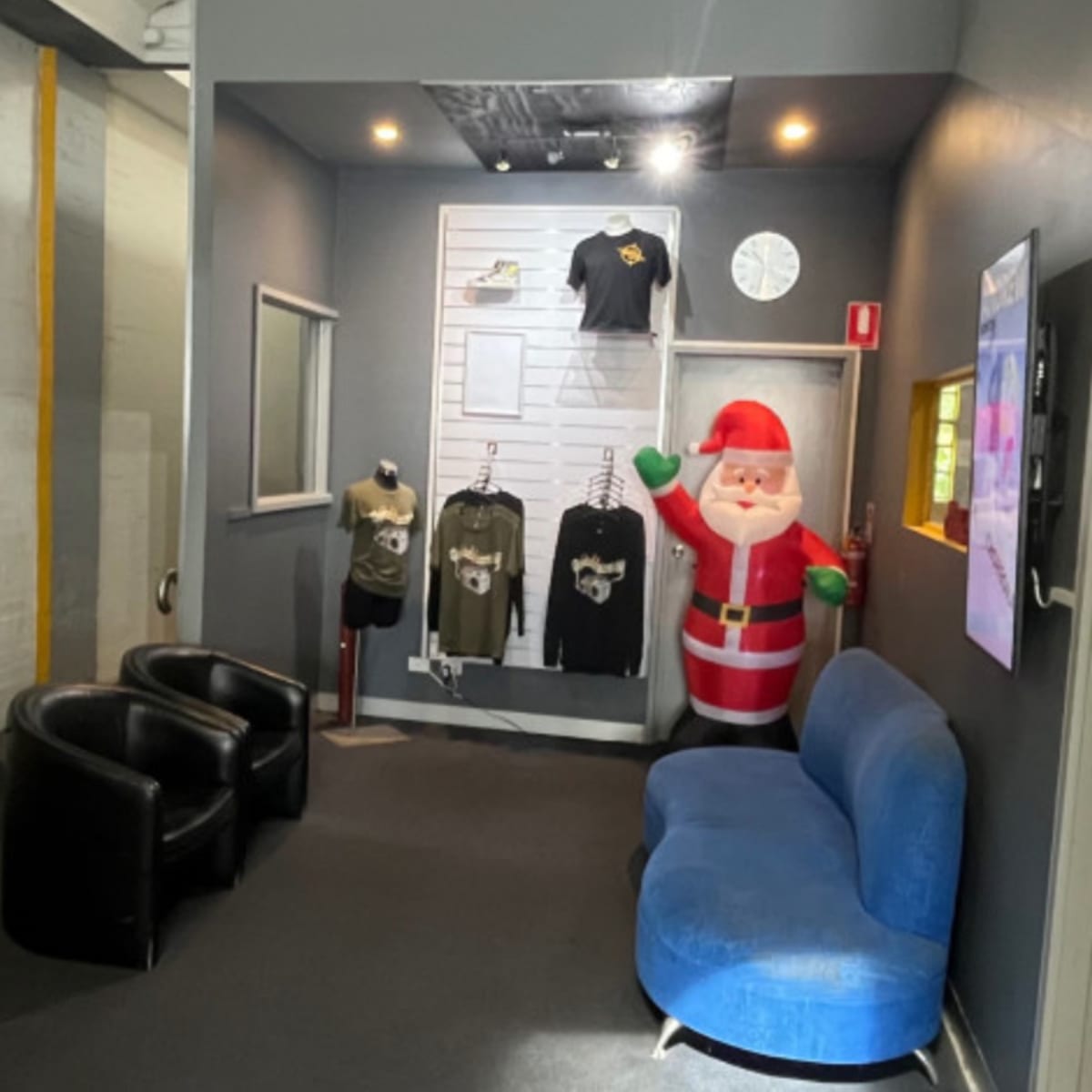 A reception area with a blue couch, two black chairs, a wall display of clothing, and a Santa Claus decoration.