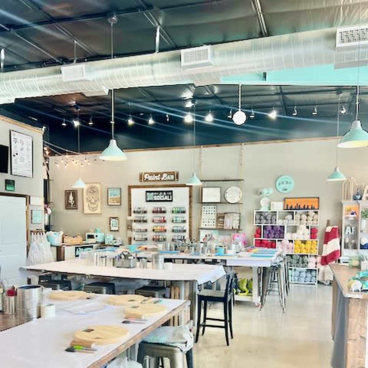 An art studio with neatly arranged tables, each equipped with painting supplies, and shelves displaying colorful craft materials.
