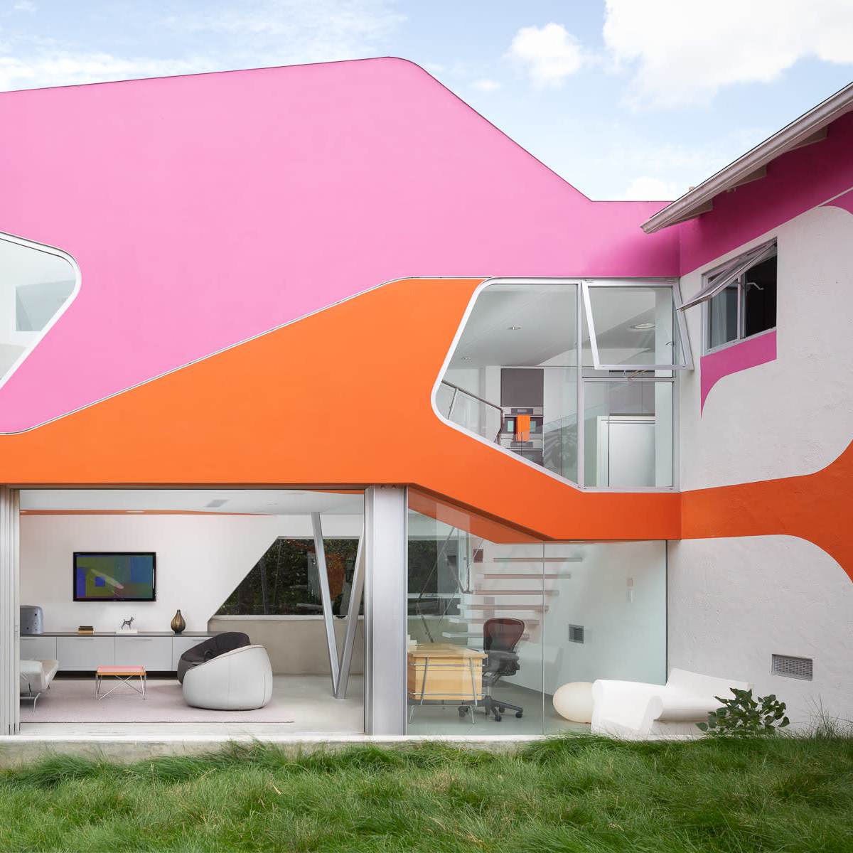 A modern house with vibrant pink and orange geometric designs on the exterior, large glass windows, and a landscaped backyard.
