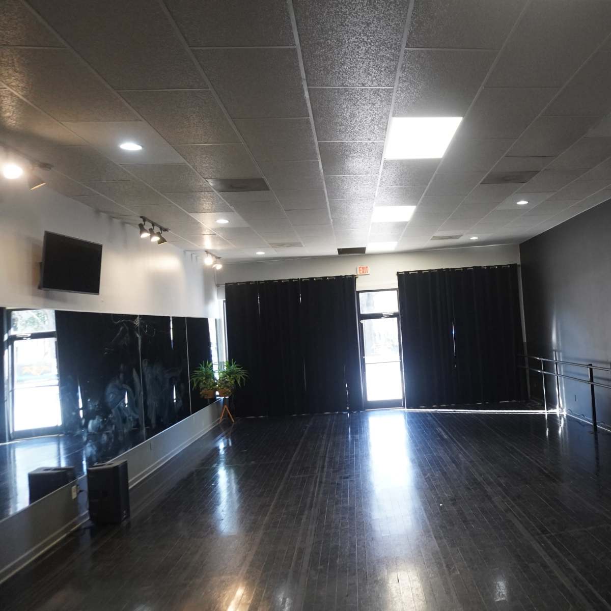 An empty dance studio with black walls, wooden flooring, a wall-mounted mirror, and a logo on the wall.
