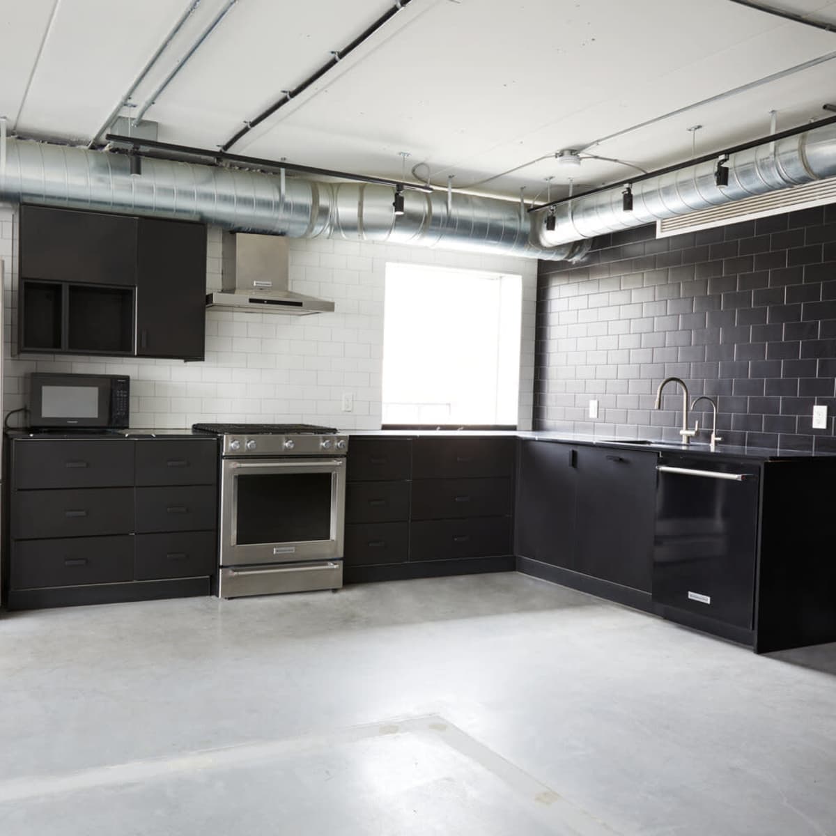 A modern kitchen featuring stainless steel appliances, black cabinetry, and a minimalist design with exposed ductwork.