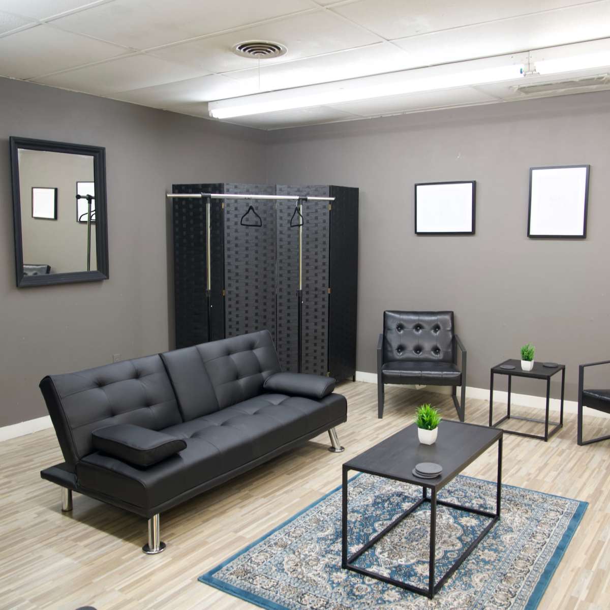 A modern, minimalist waiting room with a black sofa, two black chairs, a coffee table, and framed pictures on the walls.