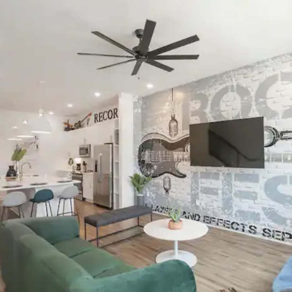 A modern, open-concept living space with a dark gray accent wall featuring large musical-themed graphics, a seating area with a blue couch and green chairs, and a dining area visible in the background.