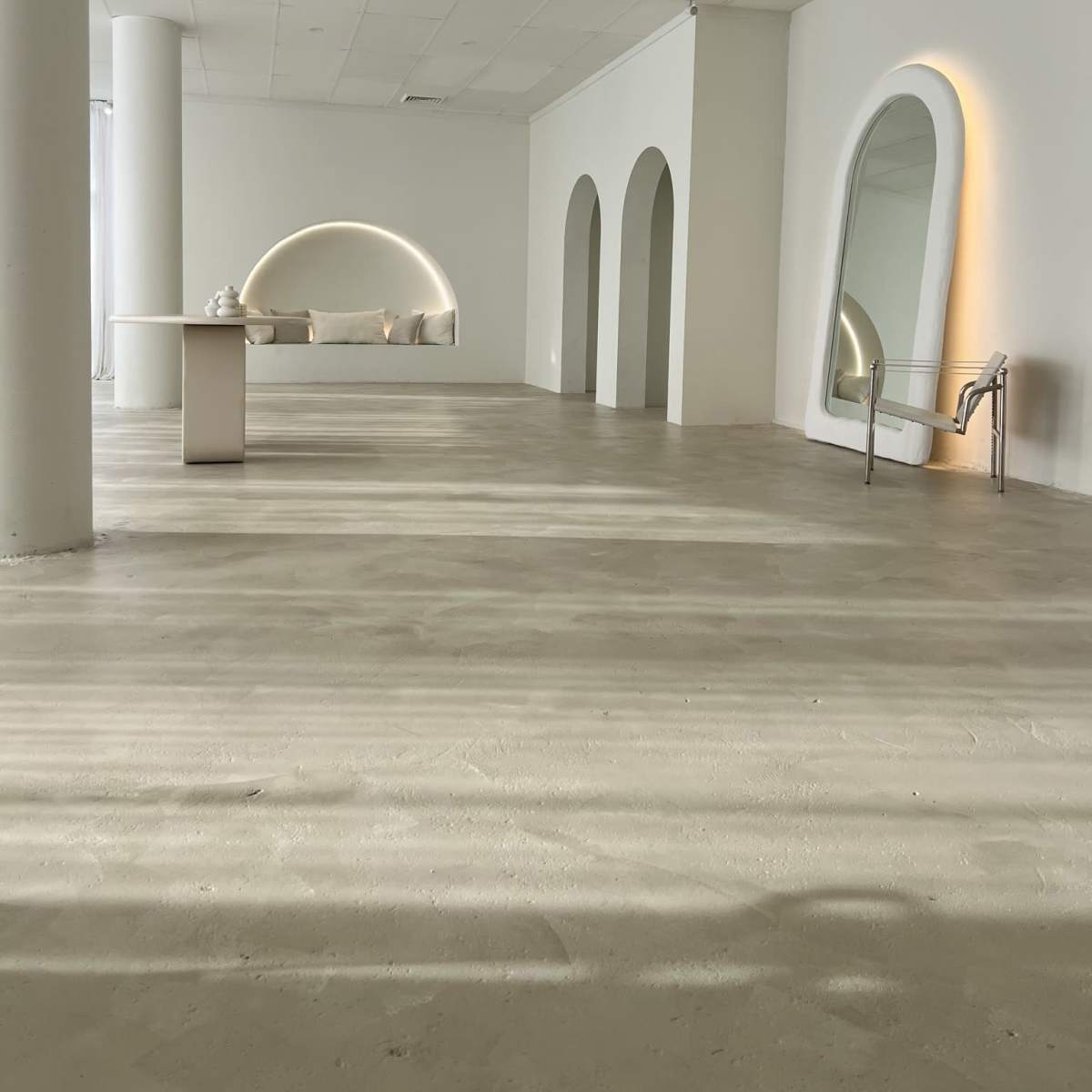A spacious, minimalist room with white walls, arched openings, and a small table along one side.