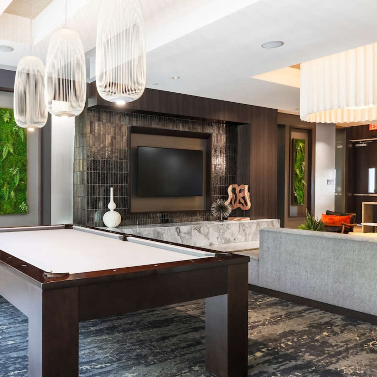 A modern lounge area featuring a billiard table, minimalist furniture, and decorative wall features, along with a large television and stylish lighting fixtures.