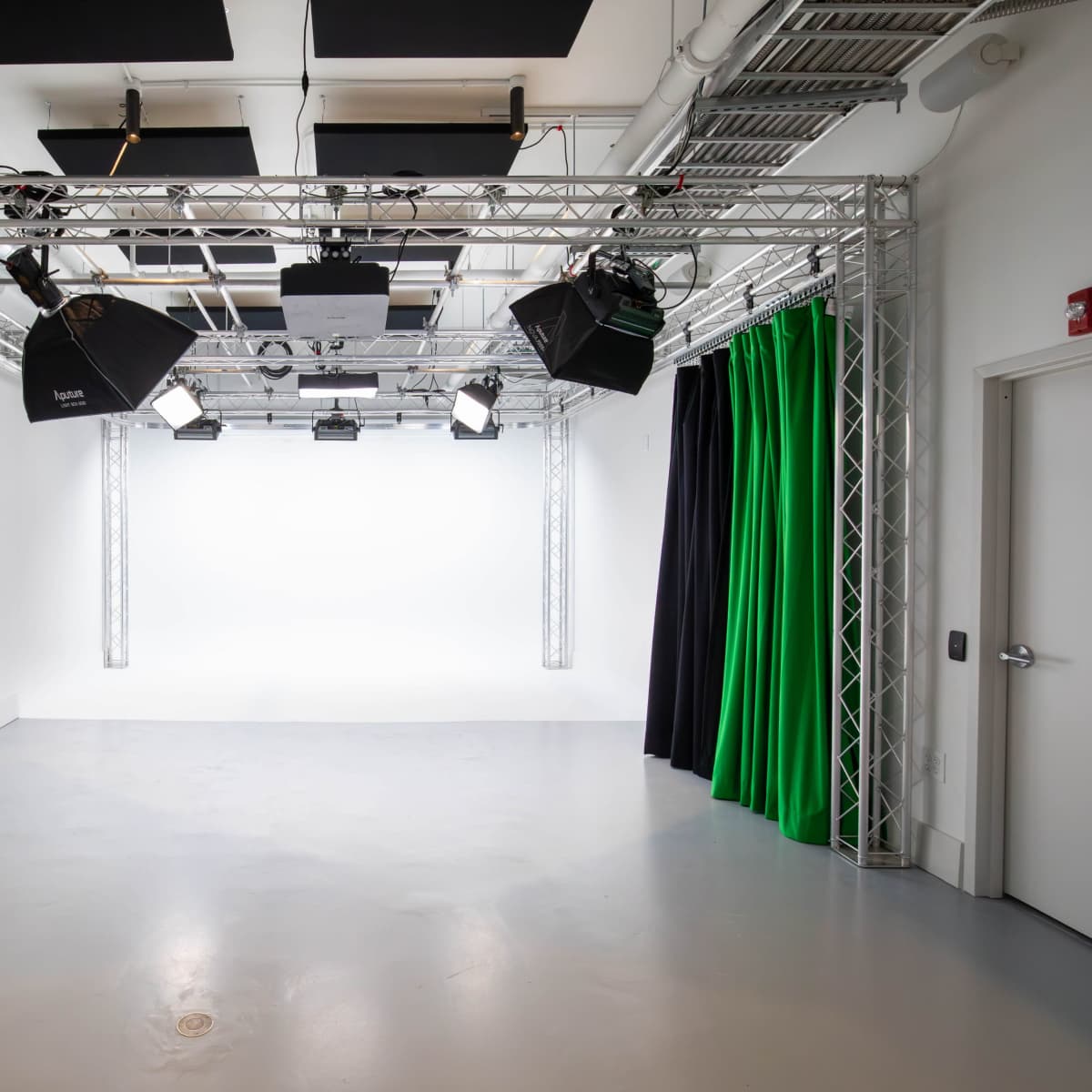 A photography studio with a white backdrop, multiple lighting fixtures, and green and black curtains.