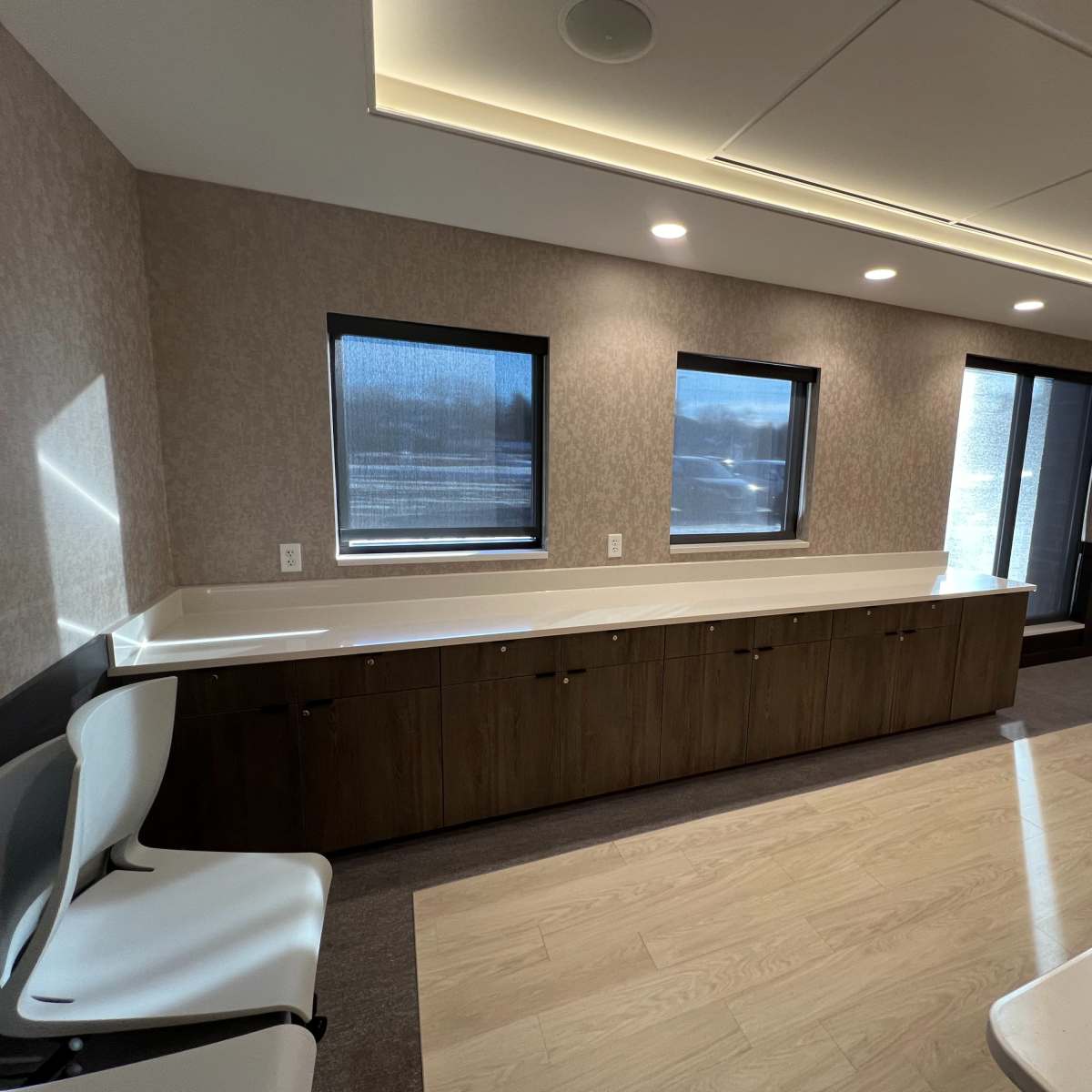 A modern room with two chairs, a long counter with cabinets below, and several windows.
