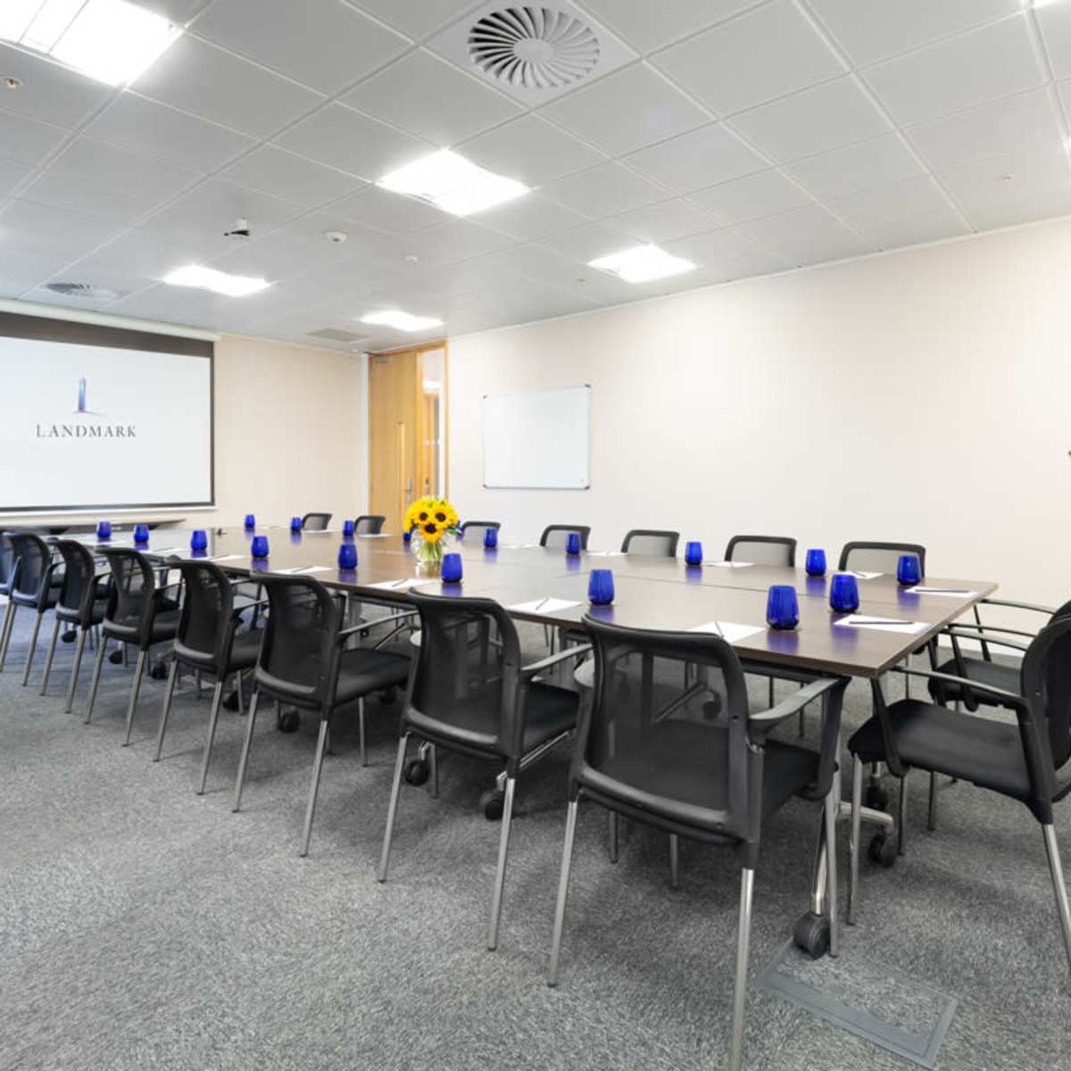 A modern conference room with a long table surrounded by black chairs, blue vases on the table, and a large screen displaying the word "LANDMARK."