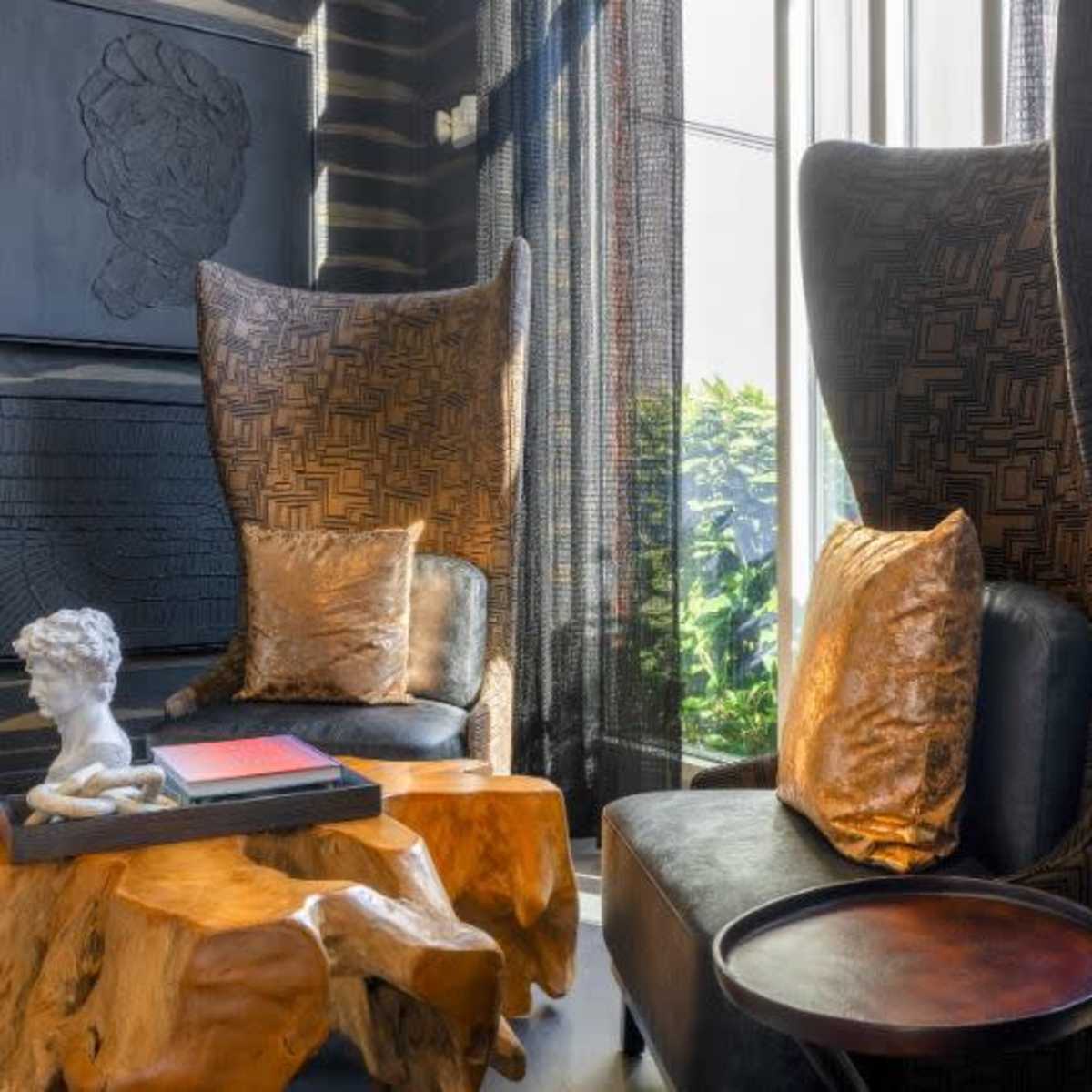 A stylish seating area featuring two tall-backed chairs, a unique wooden coffee table, and decorative art against a patterned wall.