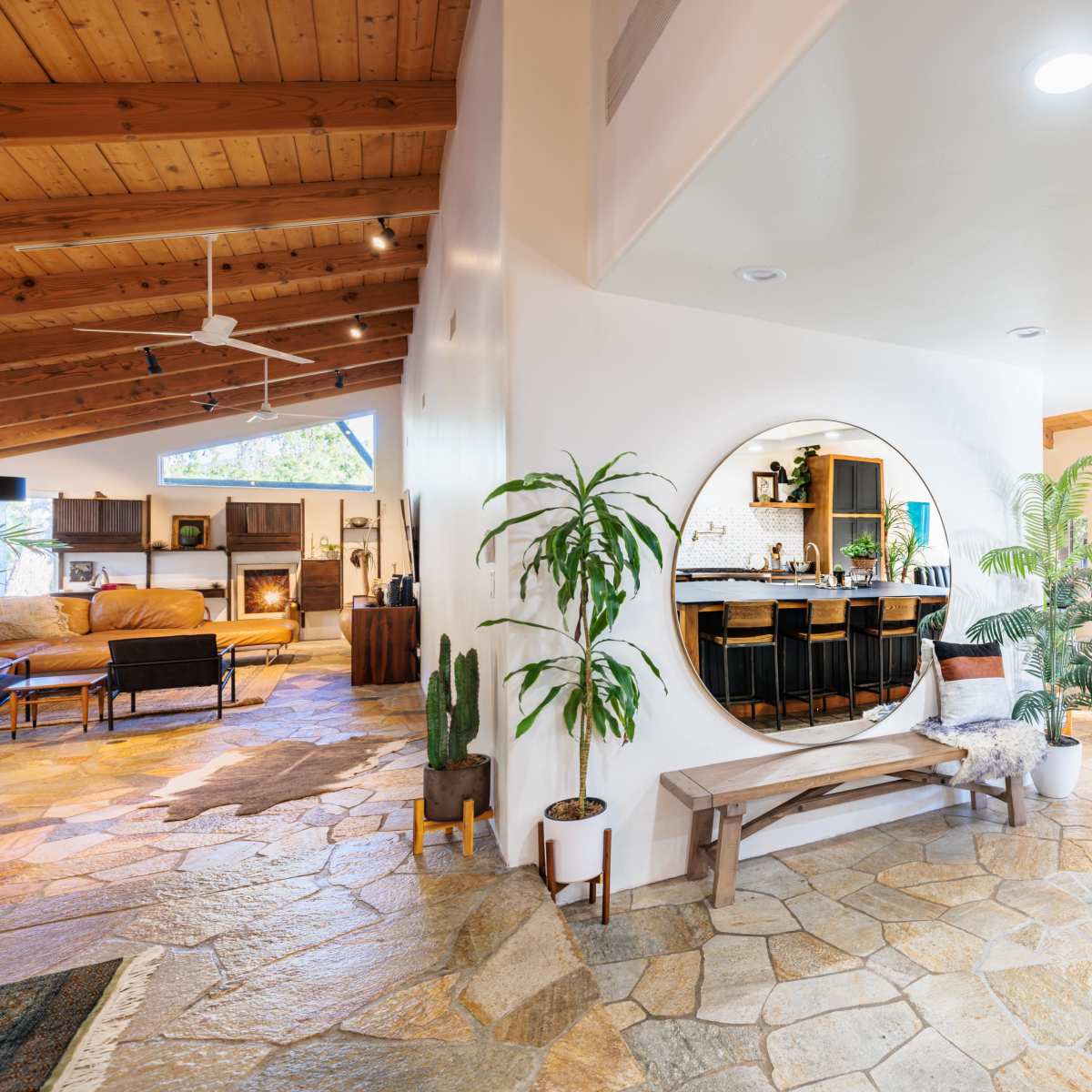 A spacious, open-concept living area with stone flooring, a circular mirror feature, and a cozy seating arrangement next to a fireplace.