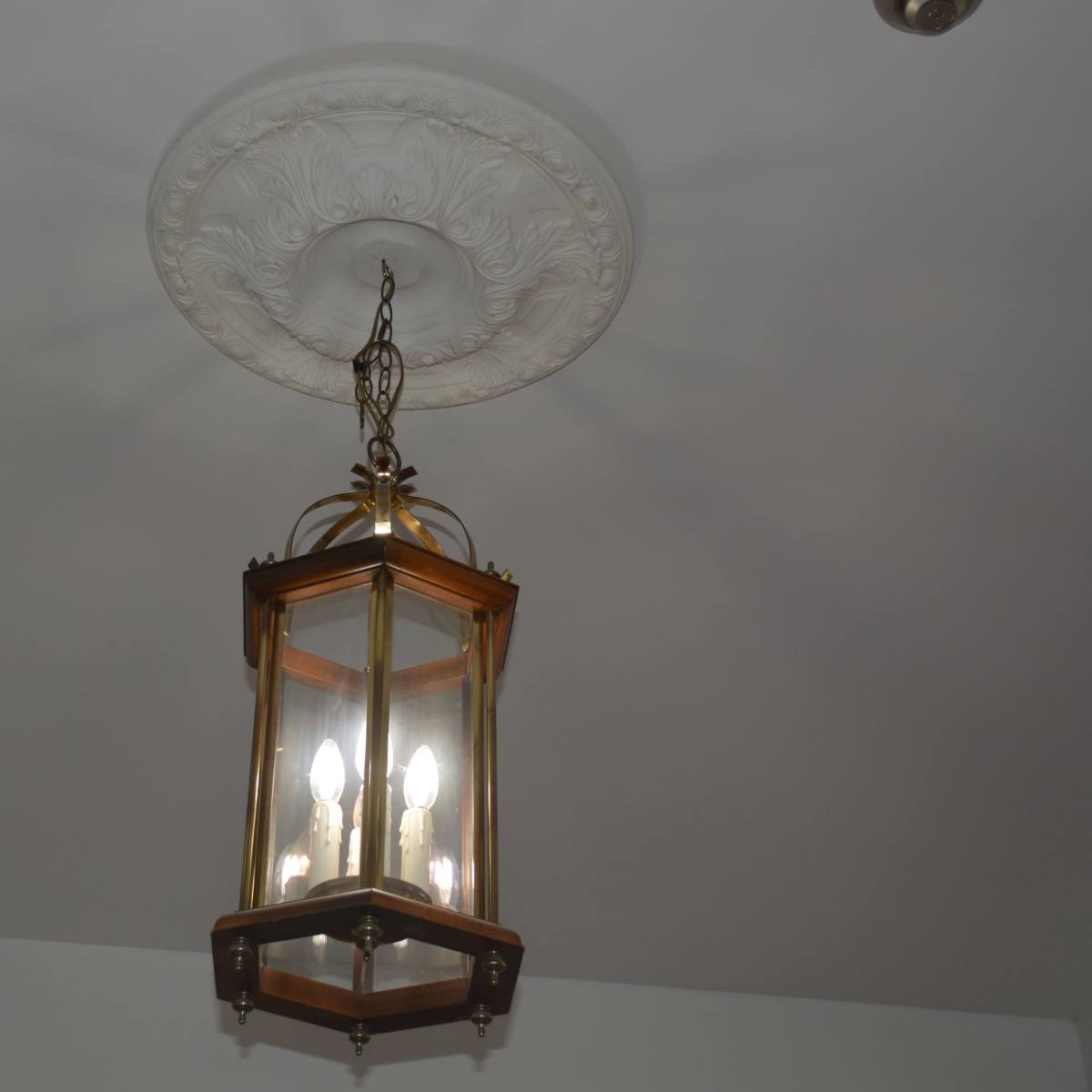 A six-sided, glass lantern hangs from a decorative ceiling medallion in a room.