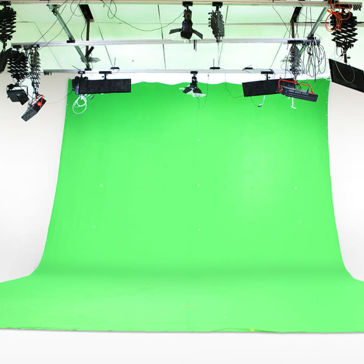 A spacious studio with a large green backdrop and various lighting equipment hanging from the ceiling.