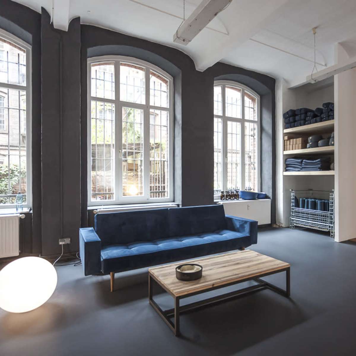 A spacious room with large windows, a blue sofa, a wooden coffee table, and shelves piled with neatly folded towels.